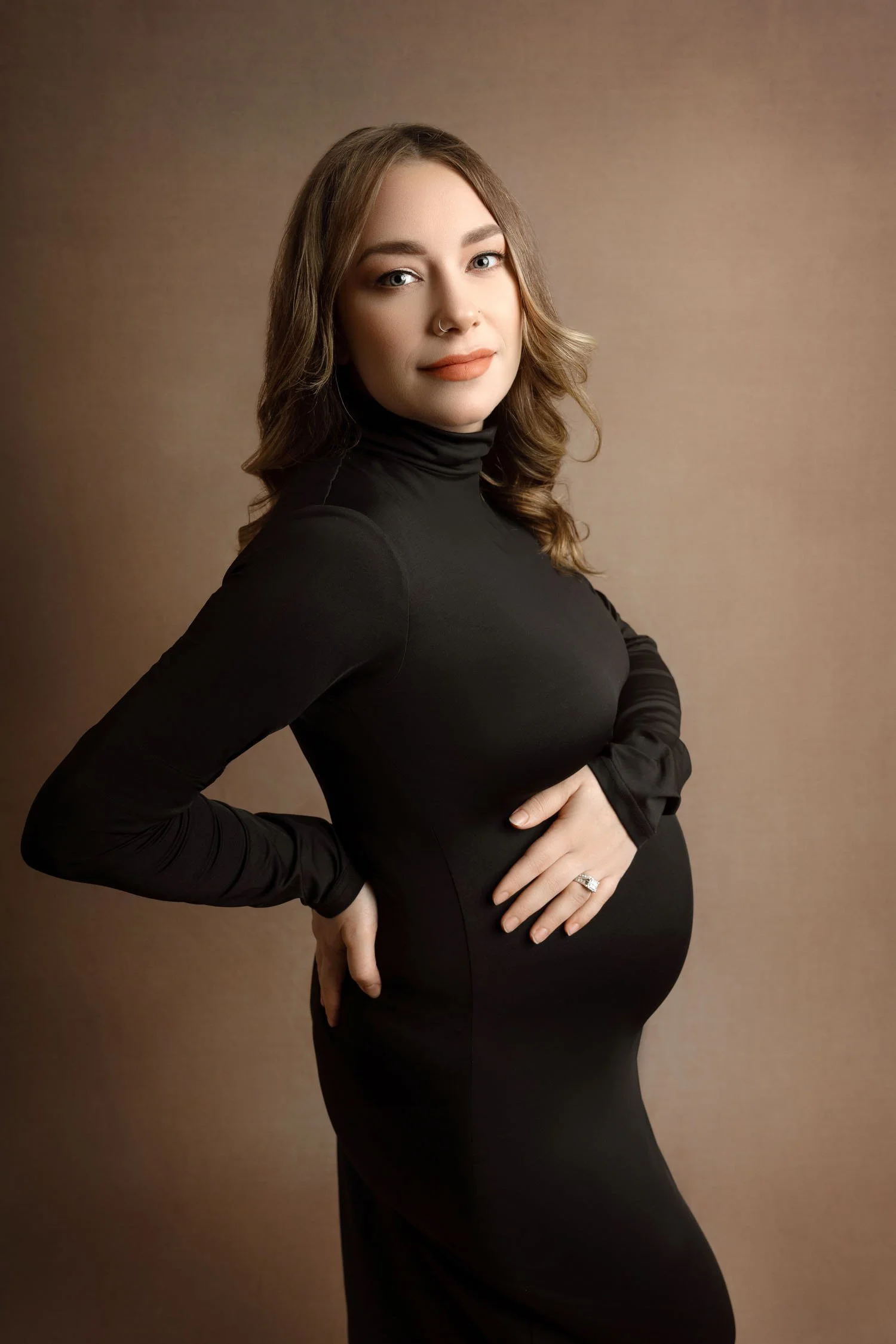 Close maternity portrait of an expecting mother wearing a fitted black dress with her hand on her baby bump.