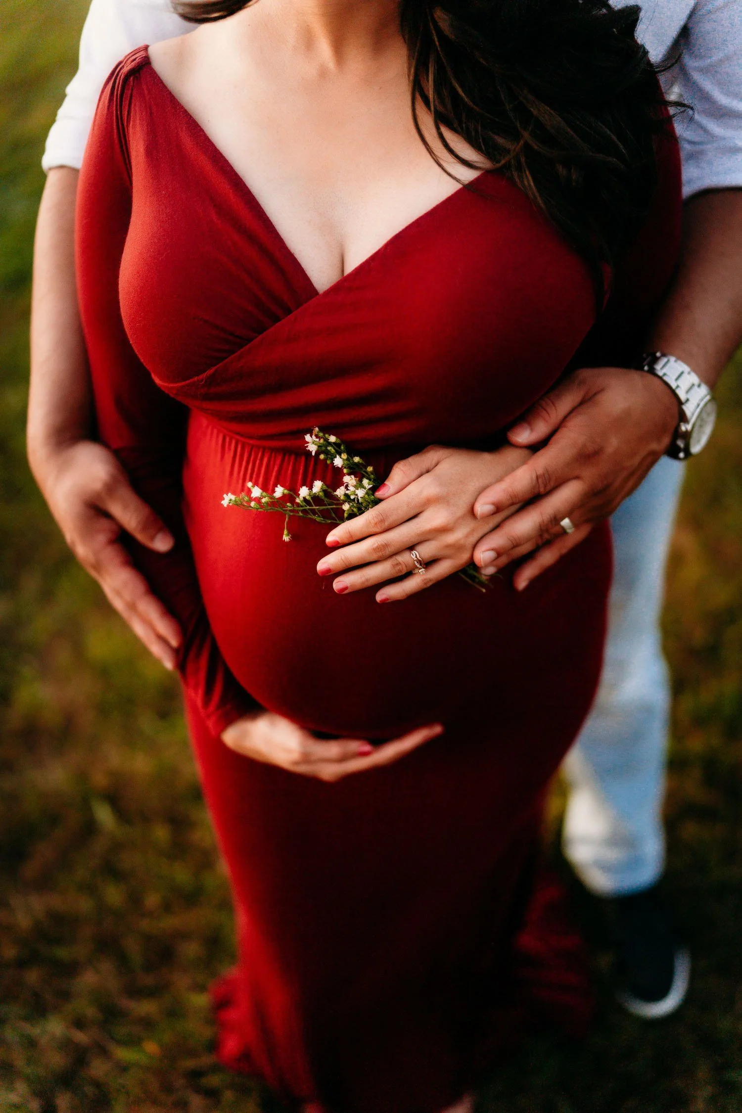 Close-up of an expecting couple holding the mother’s baby bump while she wears a fitted red gown.