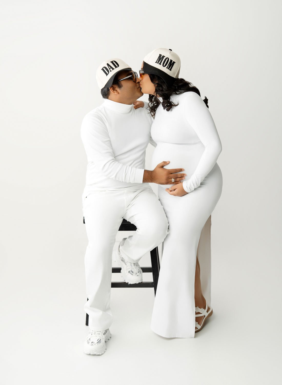 Expecting couple dressed in white posing together during a studio maternity portrait.