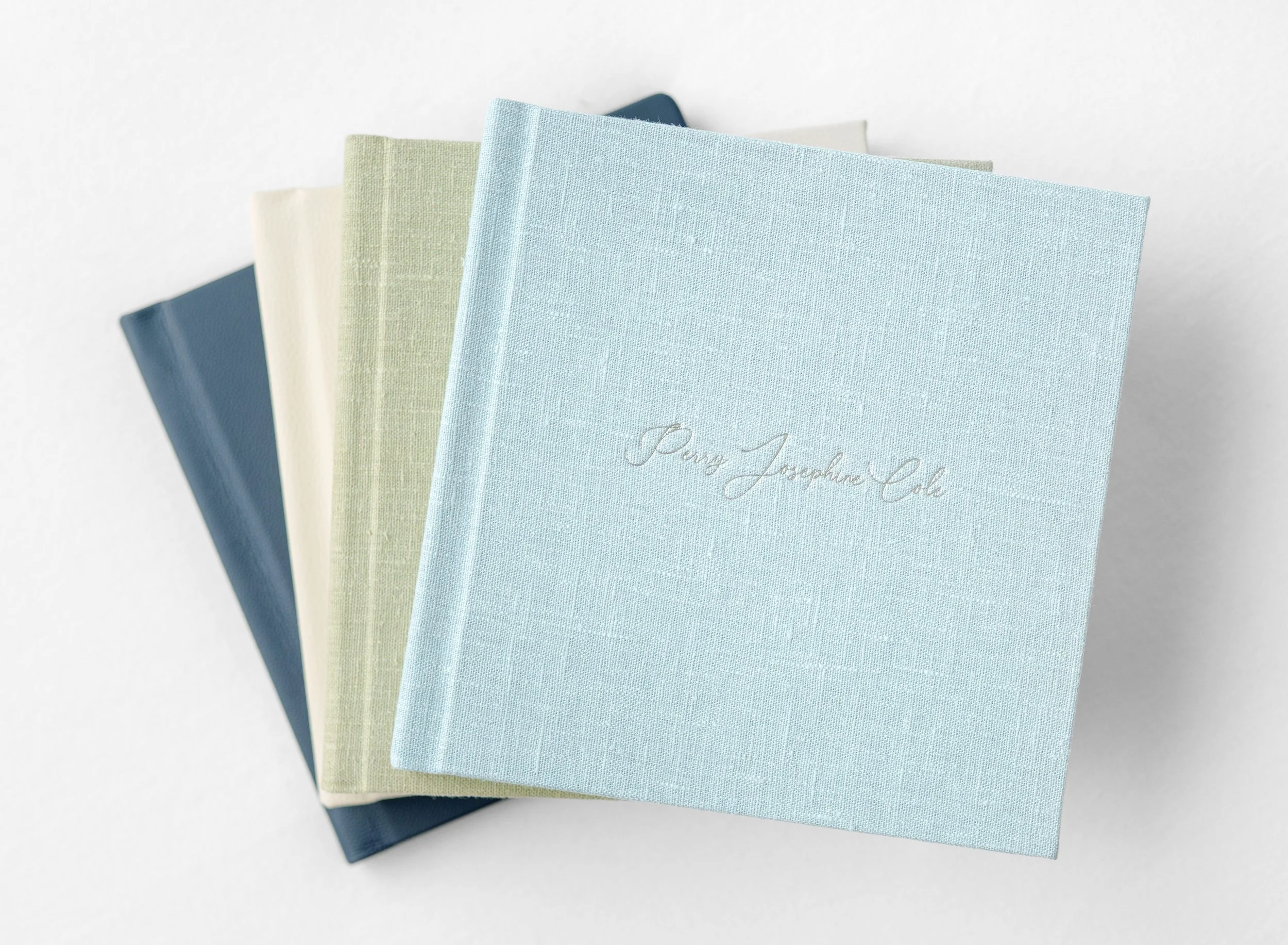 Collection of pastel linen portrait albums in soft blue, green, and neutral tones.