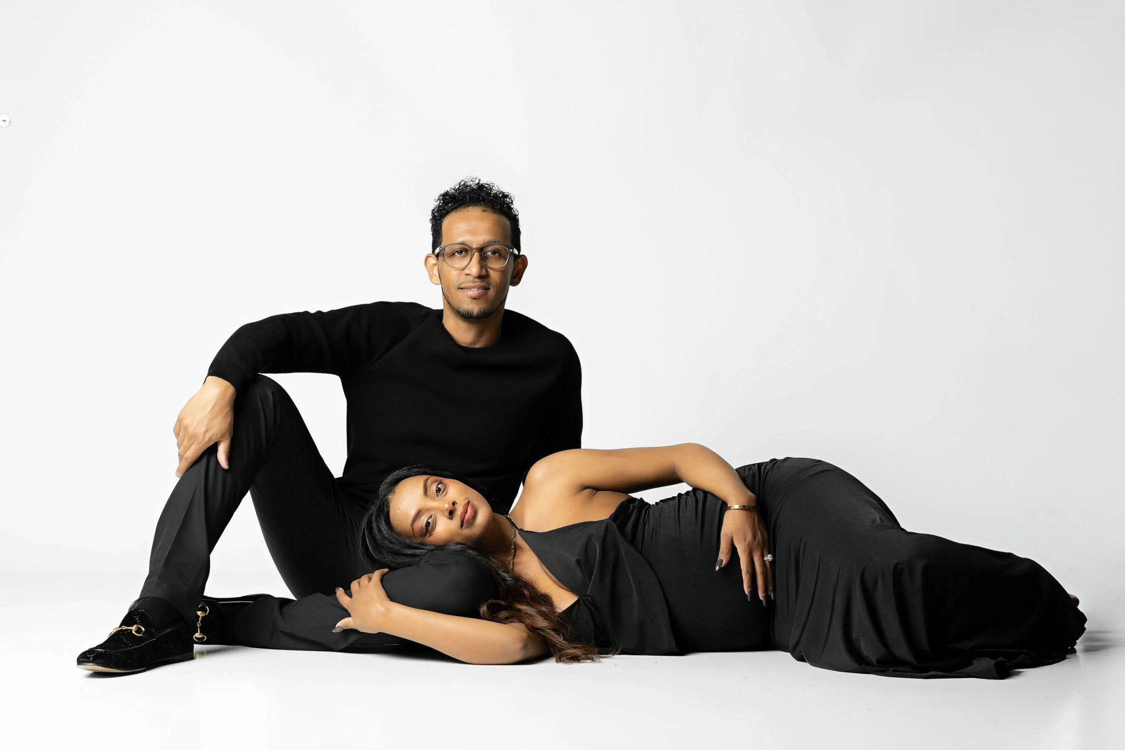 Expecting couple posing together in a relaxed studio maternity portrait.