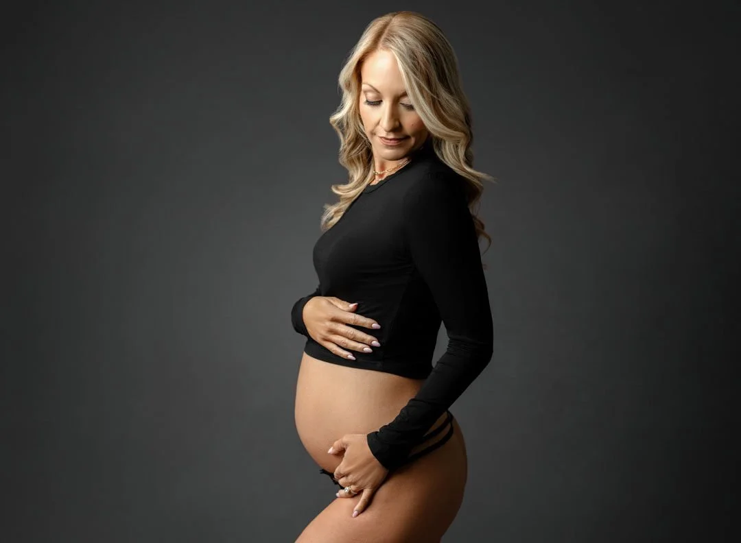 A mother to be stands in a black top and underwear smiling down to her bump after exploring Mercy birth center in st. louis