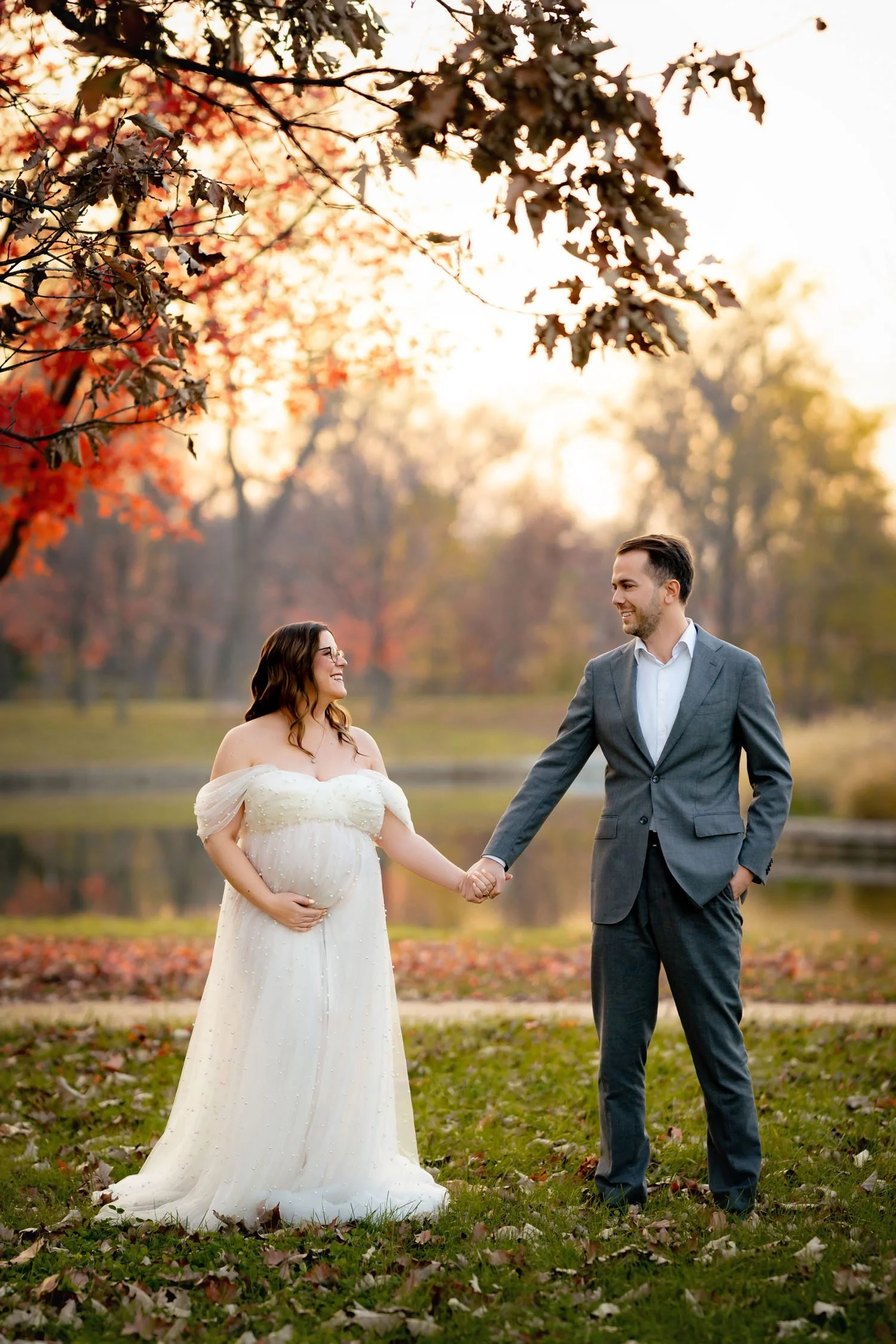 Expecting couple holding hands beneath autumn trees during a maternity session in Forest Park, St. Louis.
