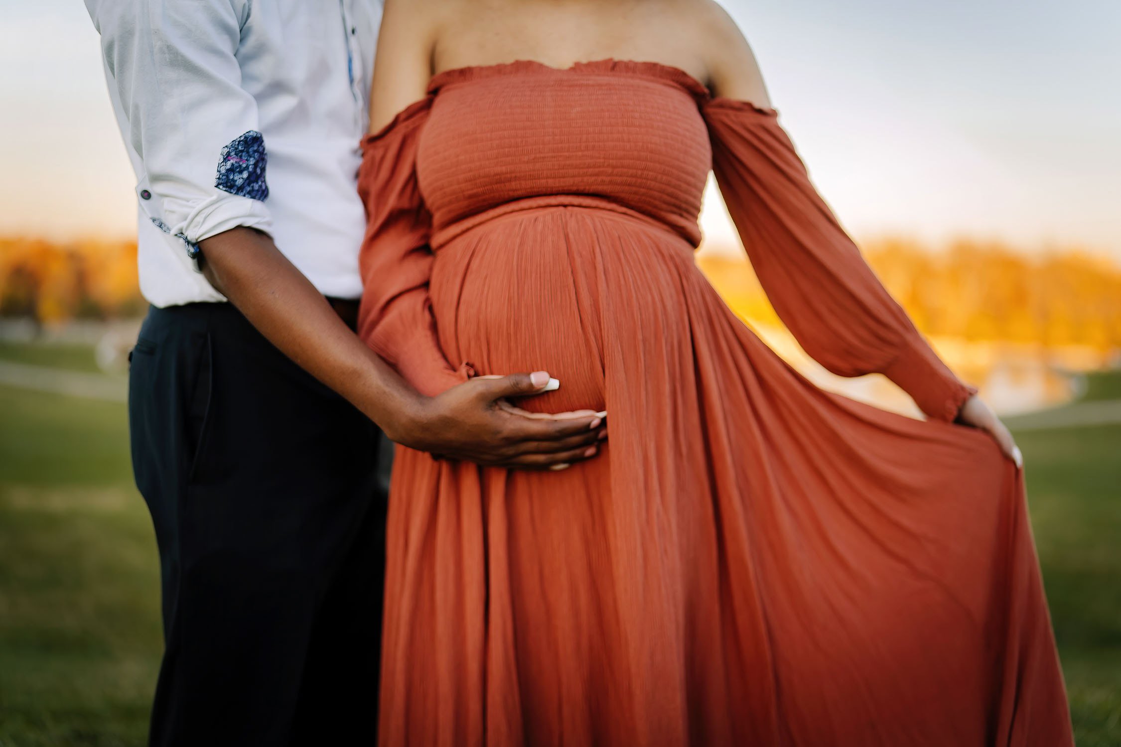 Close-up of expecting parents holding the mother’s baby bump during a sunset maternity portrait.