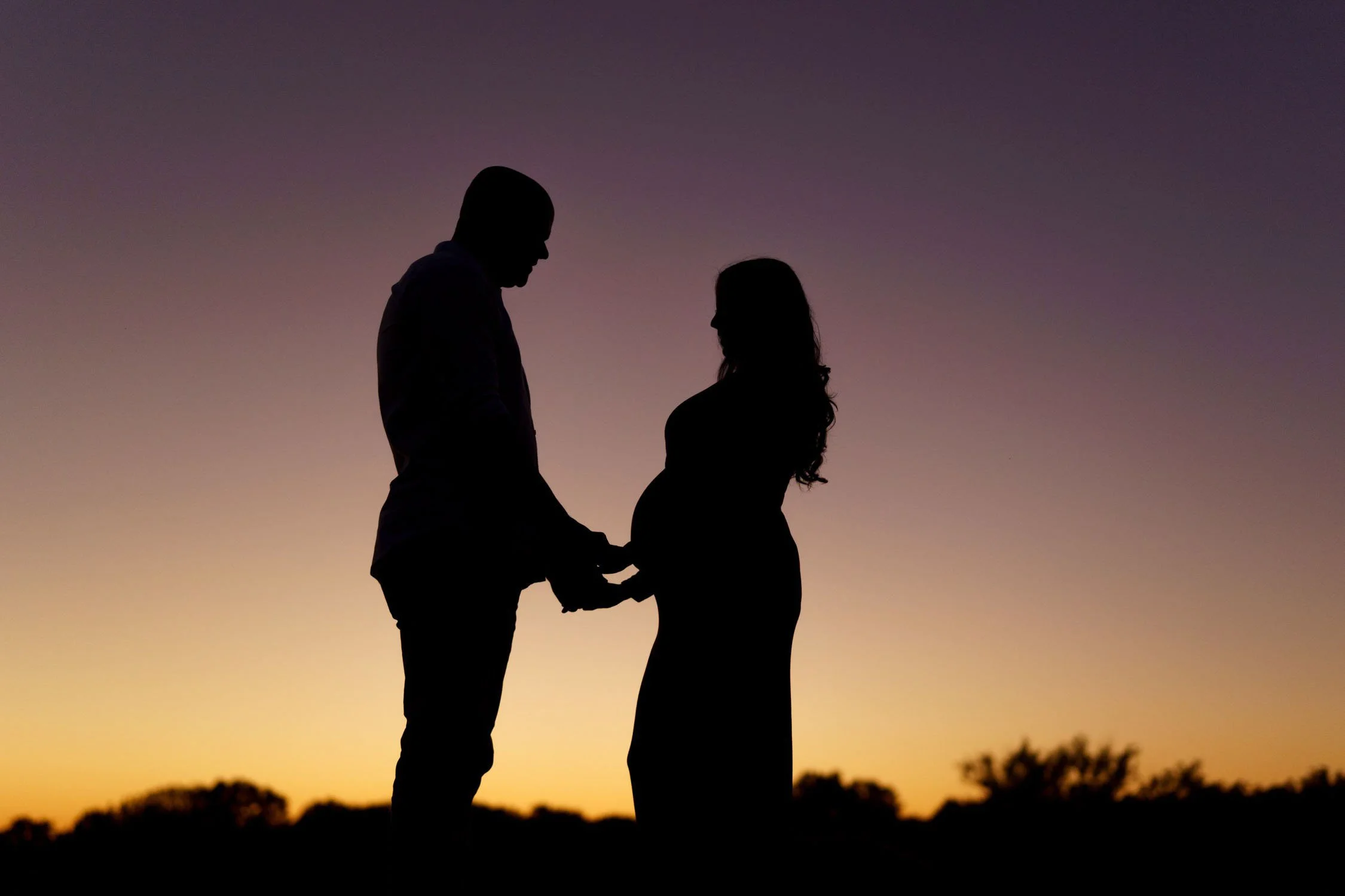 Silhouette of an expecting couple holding hands at sunset during an outdoor maternity session.