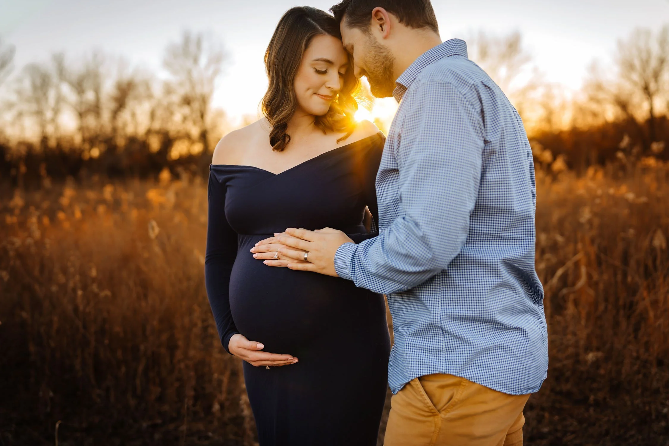 Expecting couple embracing in a field during a sunset pregnancy photography session.