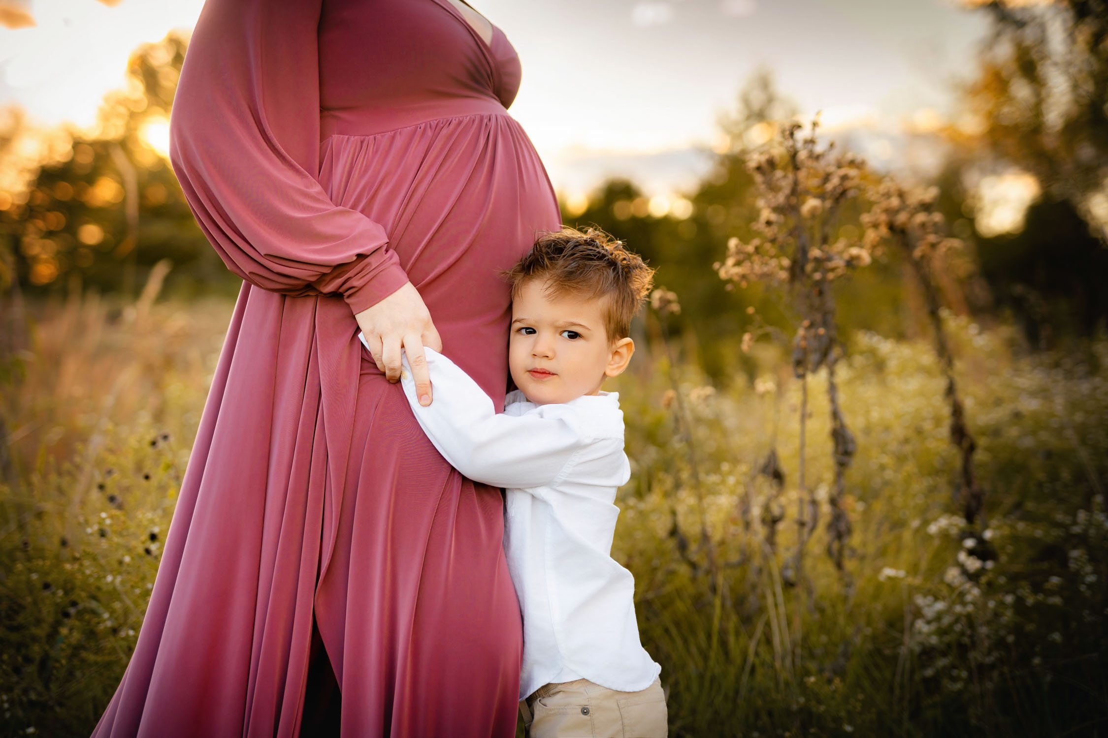 Young boy hugging his pregnant mother’s baby bump during an outdoor maternity session.