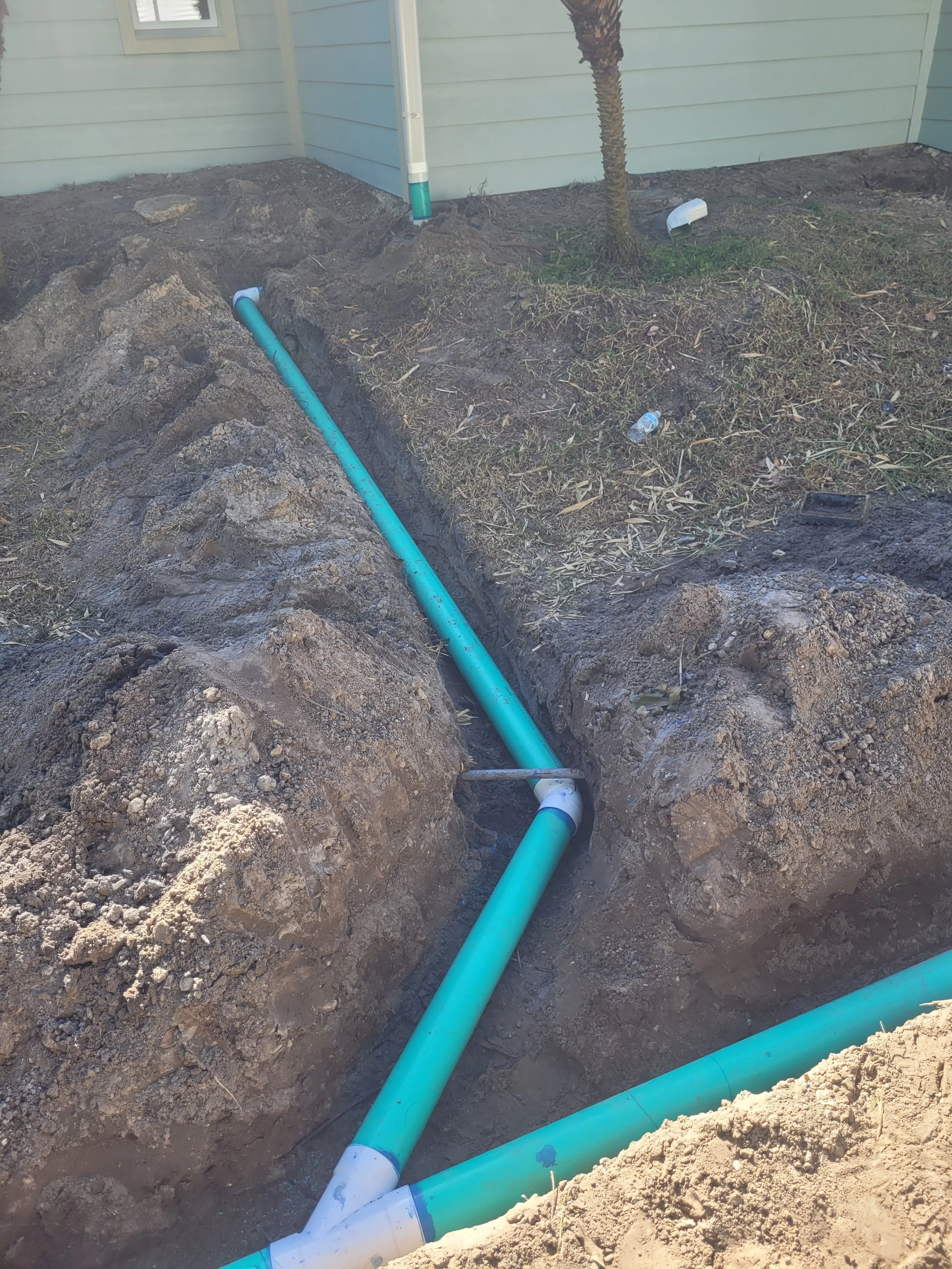 Underground plumbing pipes being installed outside a house near grass and a small tree.