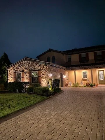 Night view of a large house with a brick driveway and well-maintained garden.