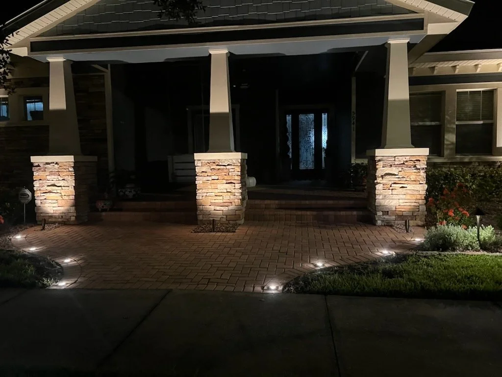 Night view of a house's front porch with stone columns, steps, and illuminated pathway lights.