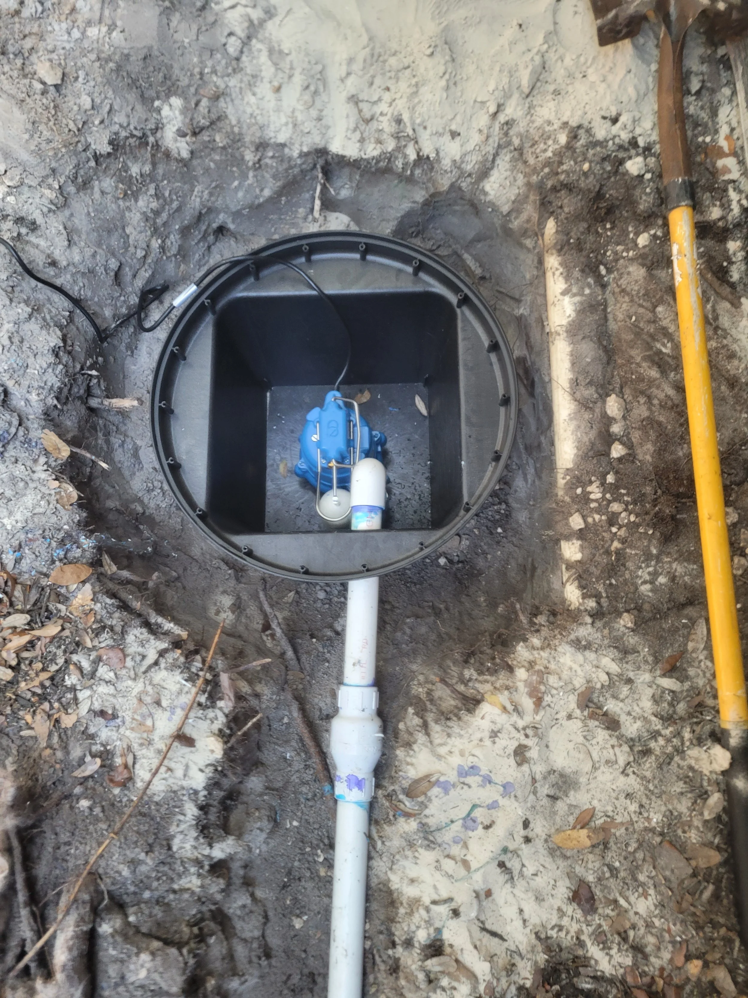 Underground plumbing system with a check valve and a pump installed in a circular excavation in the ground.