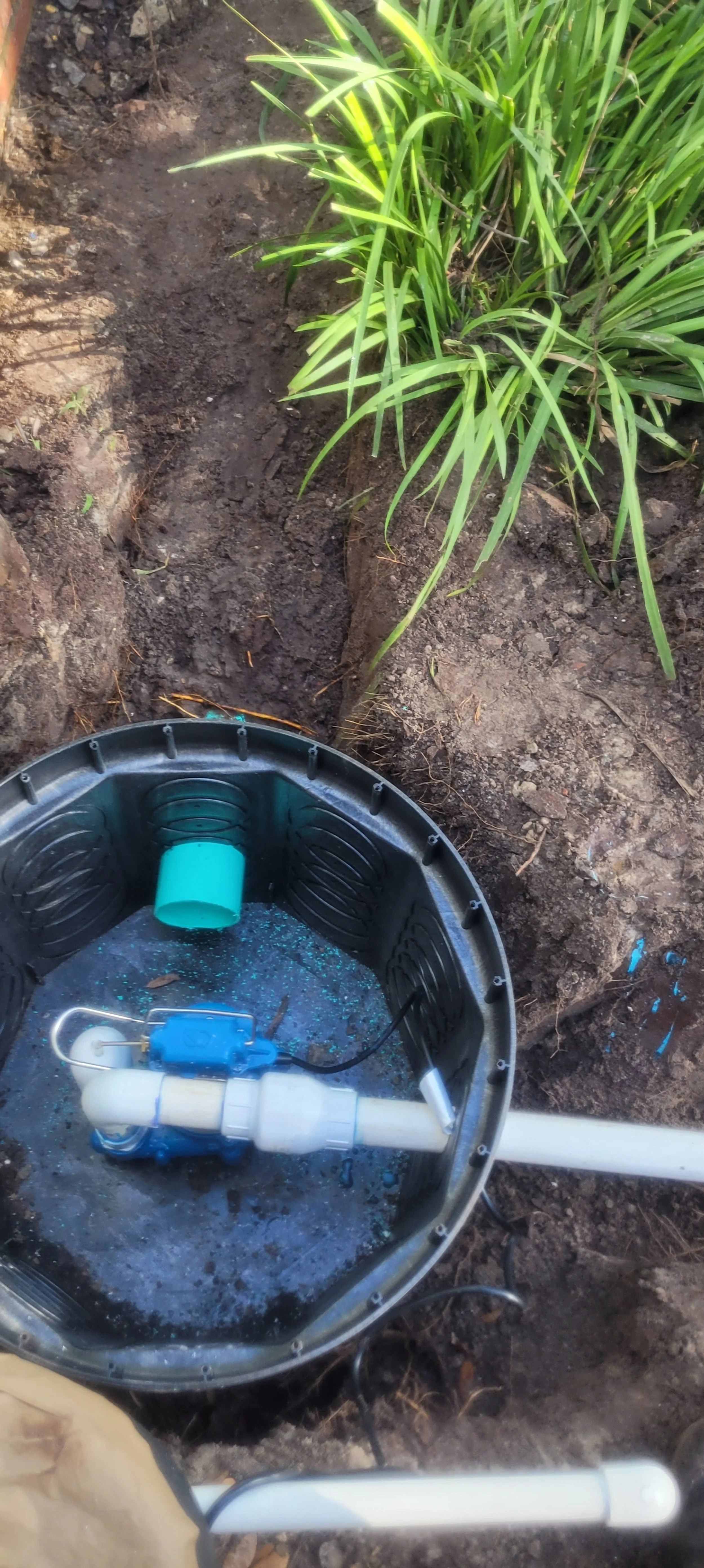 A backyard irrigation pump system installed in an outdoor garden area with brown soil and green plants.