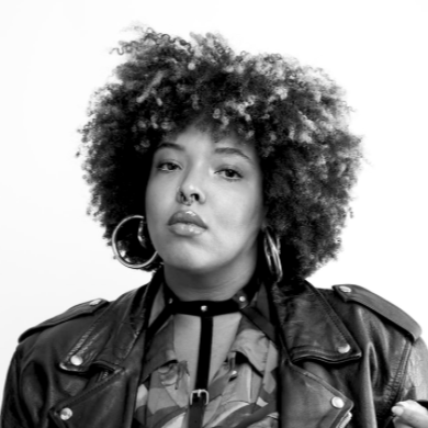 Black and white portrait of a woman with curly hair wearing a leather jacket and hoop earrings.