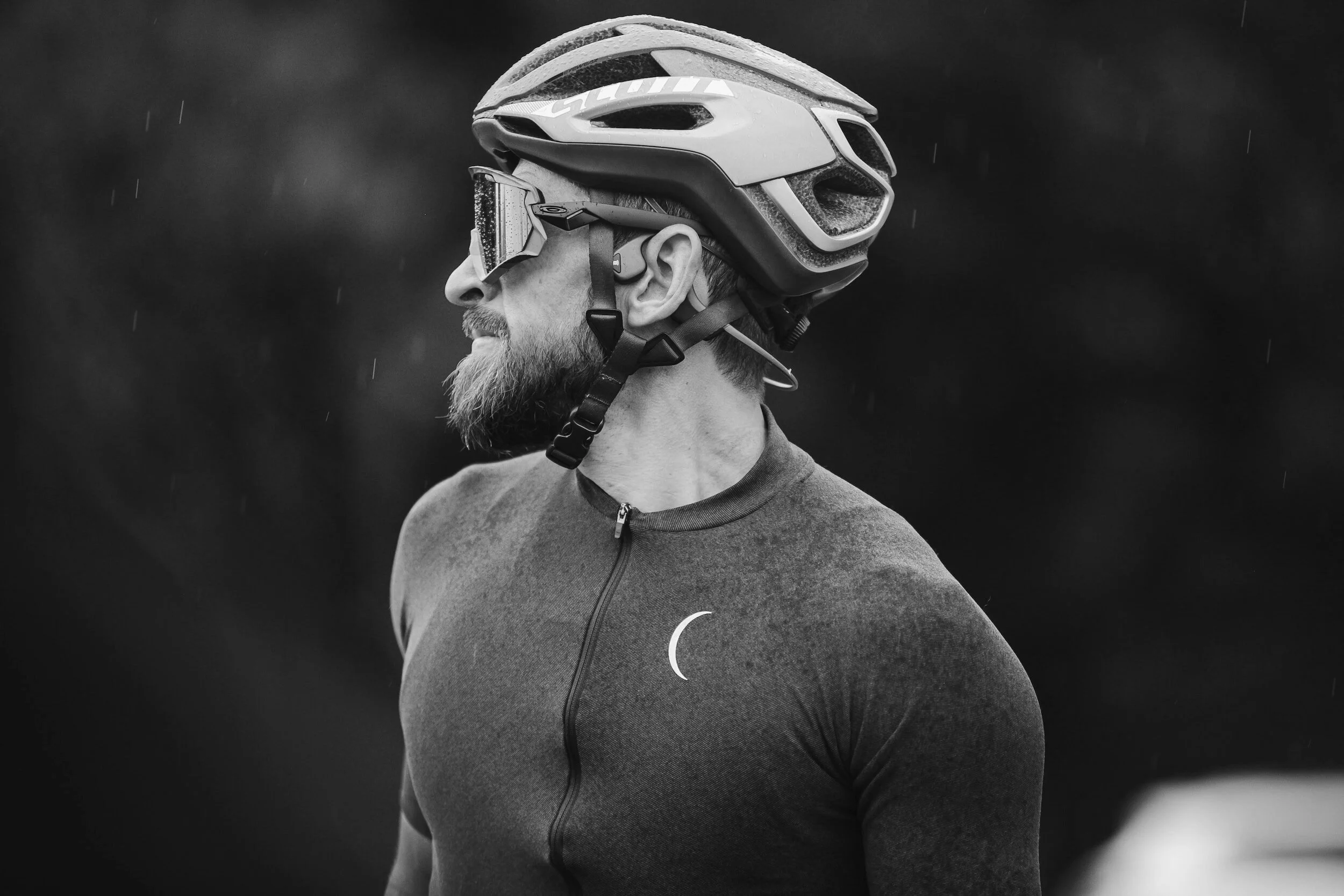 Side profile of a man wearing a bike helmet, goggles, and athletic clothing during rain.