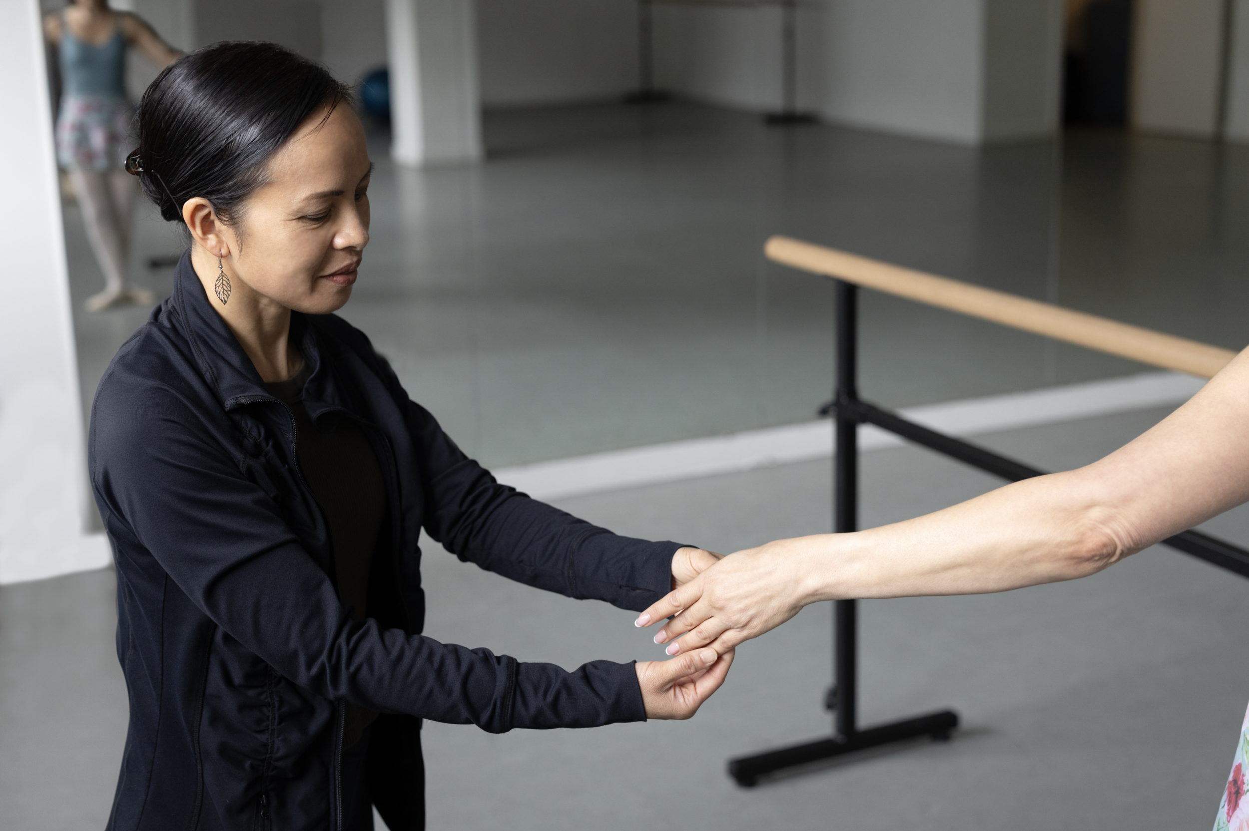 A woman in a black jacket shaking hands with another person whose arm is extended toward her.