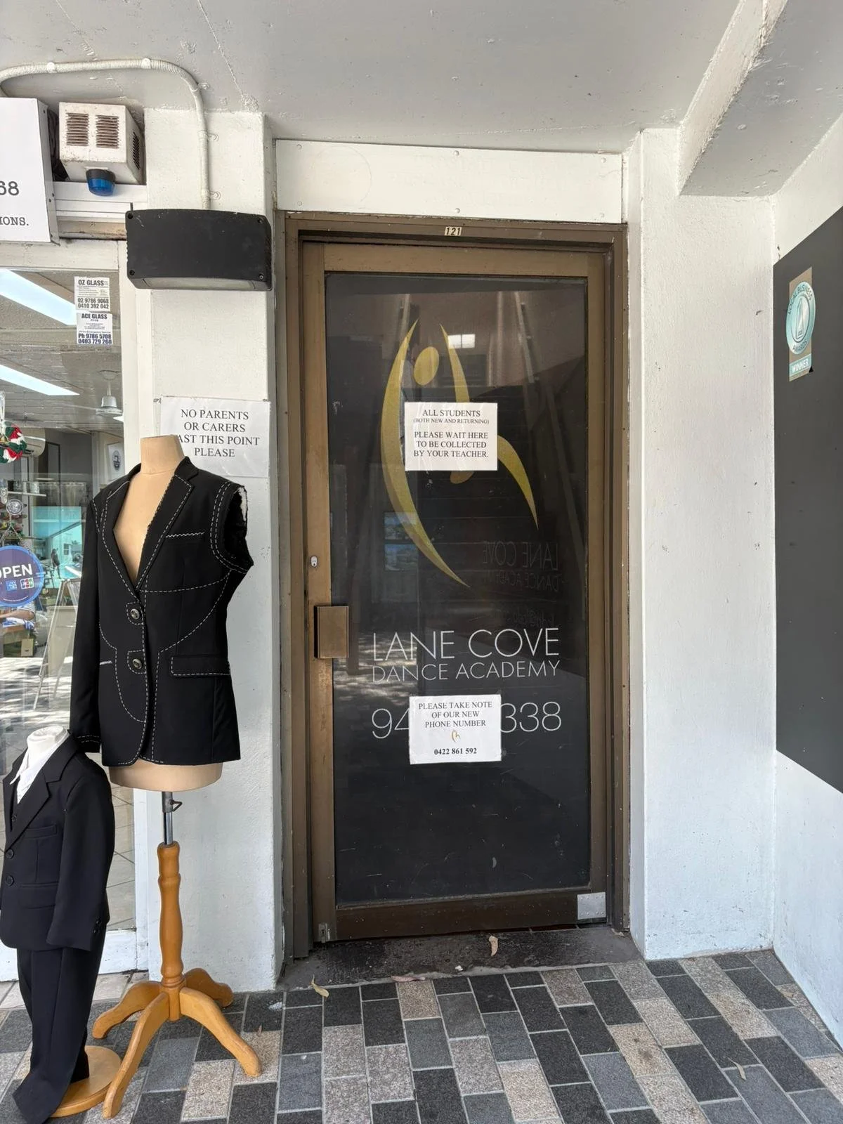 Entrance door to Lane Cove Dance Academy with signs and mannequins displaying business attire outside.