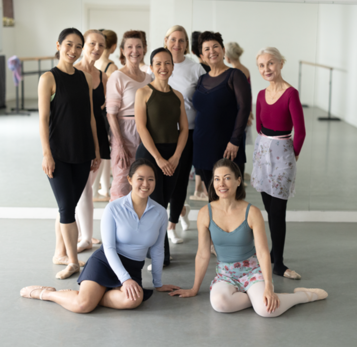 Group of women in ballet attire and dancewear posing in a studio with a mirror.