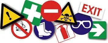 Collection of safety and hazard symbols including warning signs, exit sign, first aid symbol and prohibition icons, representing health and safety awareness in public spaces and events.