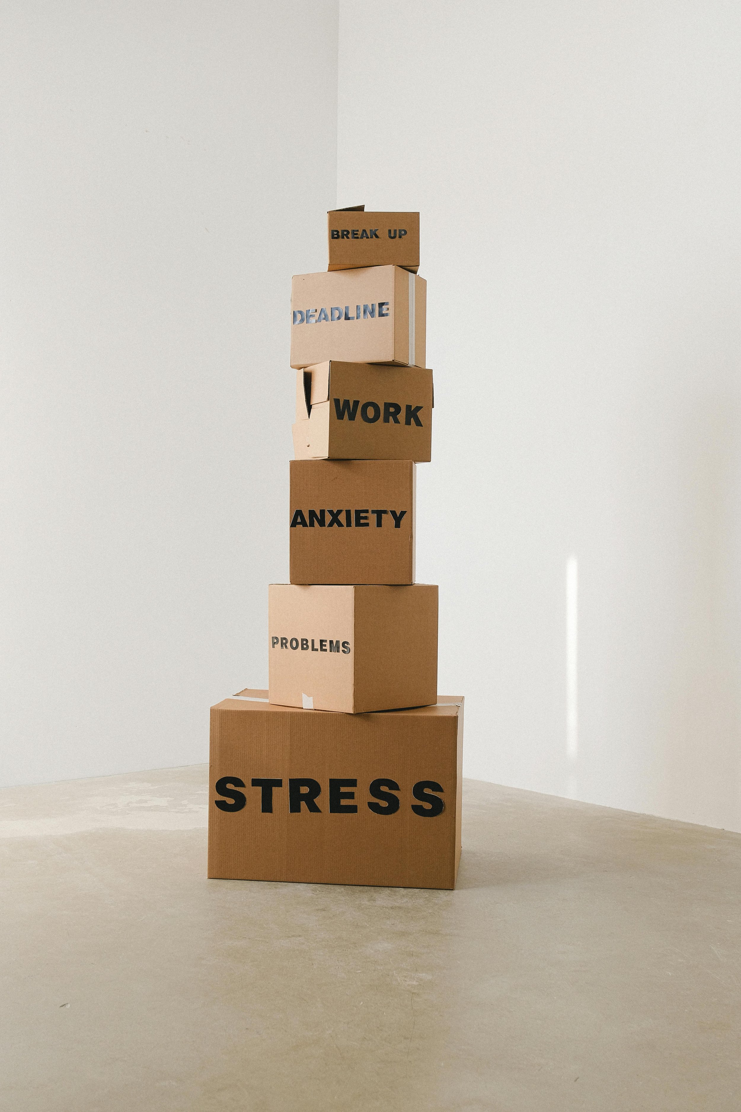Stack of boxes labelled stress, problems, anxiety, work, deadline and break up, visually representing how different pressures build up and contribute to emotional overwhelm