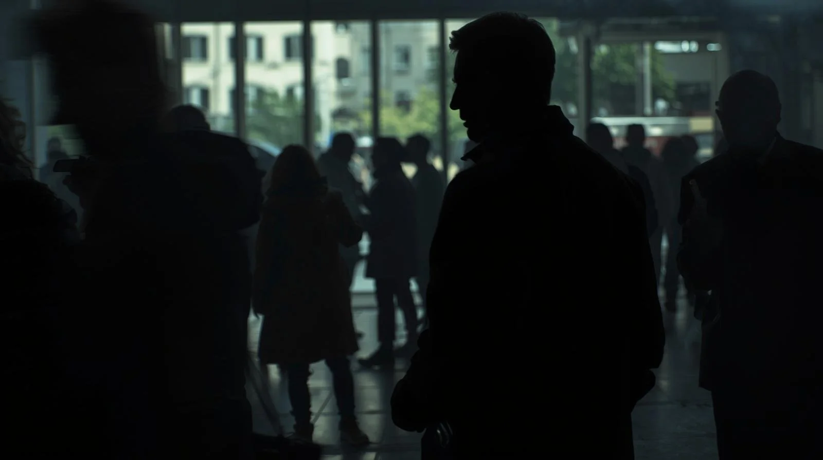 Silhouettes of people inside a building with large windows showing a cityscape outside.