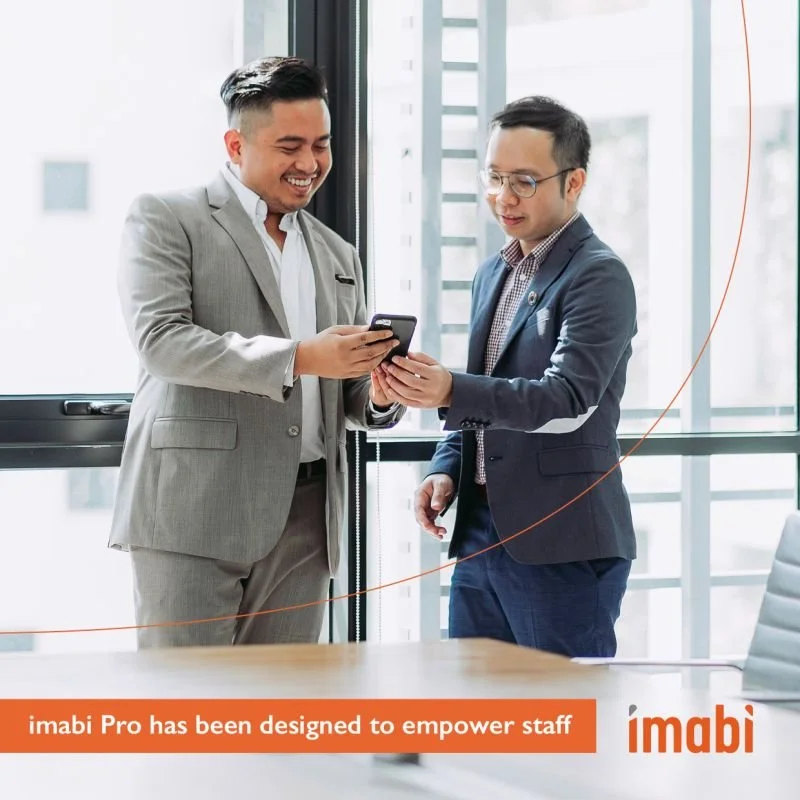 Two businessmen in suits looking at a smartphone in a modern office setting with an imabi logo and slogan.