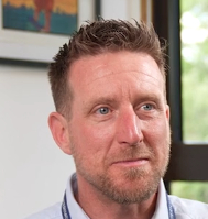 Man with a short beard and short hair sitting indoors