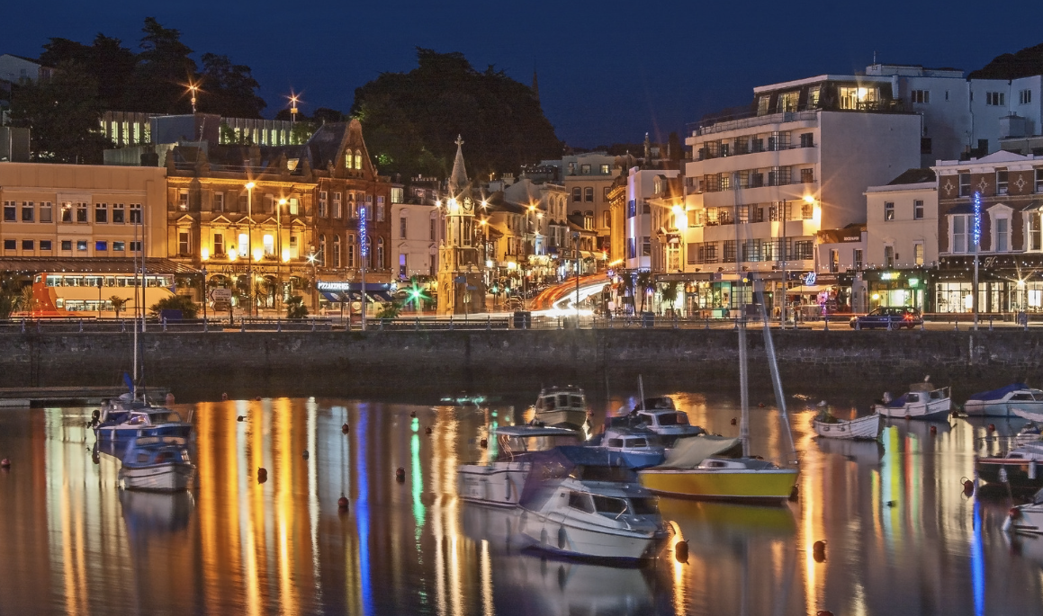 Torbay Bay at night, showing the illuminated seafront and highlighting the importance of night-time safety supported by Travel Guardian.