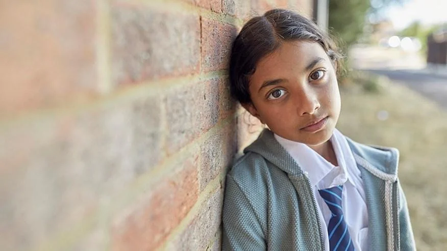 Young school-aged girl leaning against a brick wall, illustrating vulnerability and the hidden risks of child criminal exploitation, county lines grooming and the importance of early safeguarding intervention.