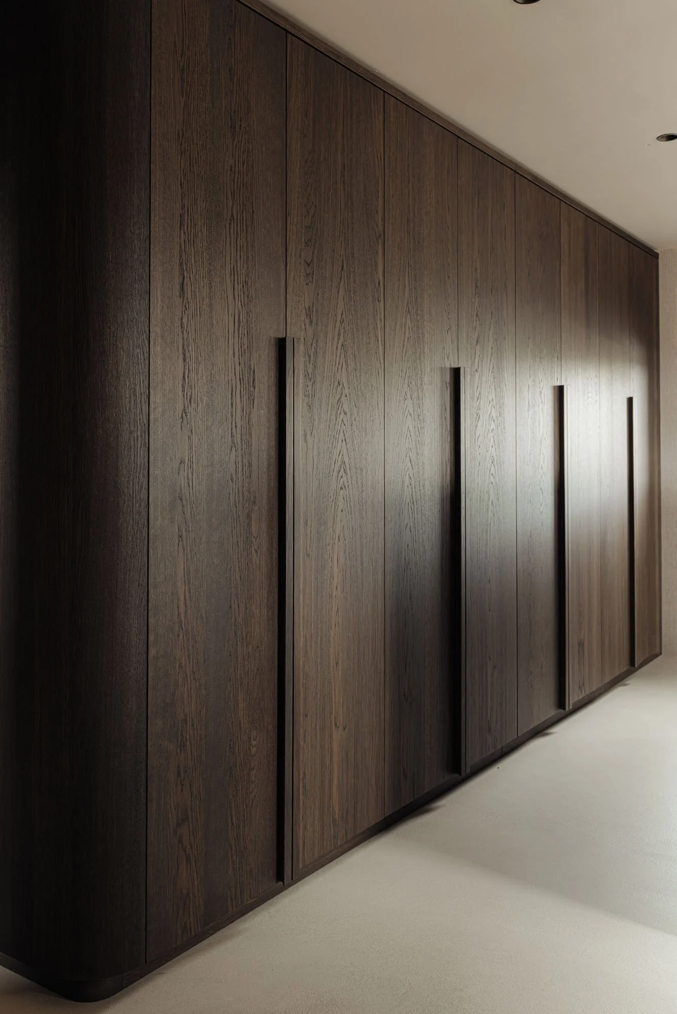 ngetogen luxe in een master bedroom met een afgeronde garderobekast op maat van donker hout, ontworpen door Studio Engelhard uit Amsterdam.