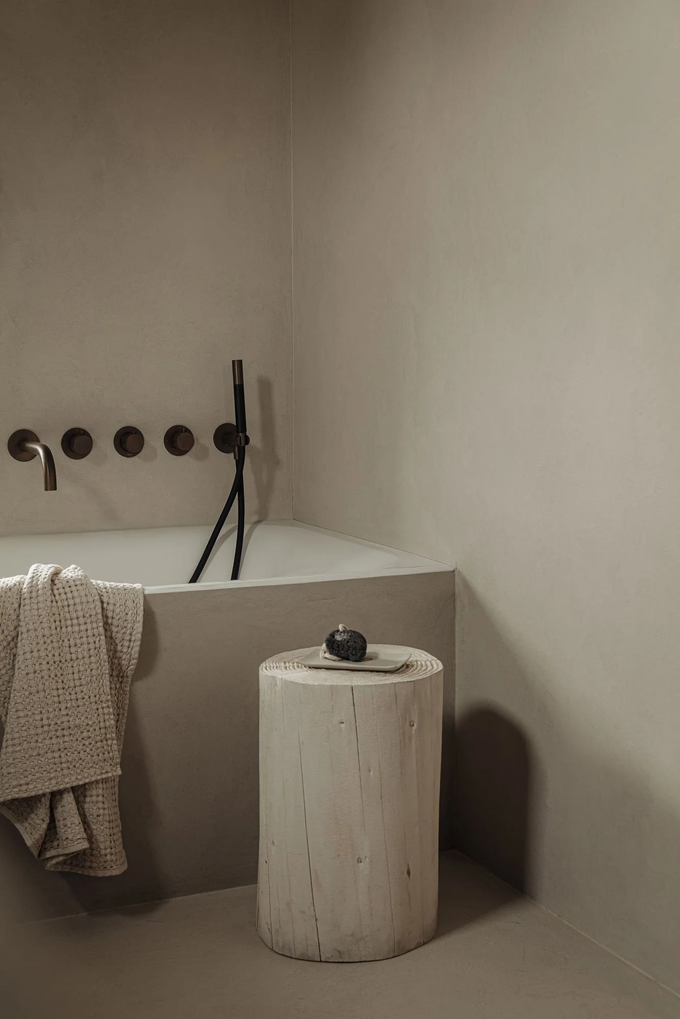 Luxe badkamer van microcement met een ingebouwd ligbad en design kranen, ontworpen in een minimalistische wellness-stijl door Studio Engelhard uit Amsterdam.