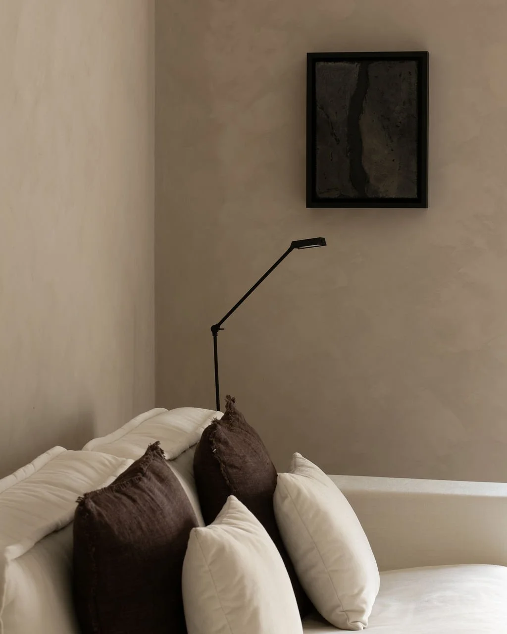 Detail van lime-painted wand en slanke zwarte leeslamp in een serene, warme woonruimte met een minimalistisch kunstwerk.