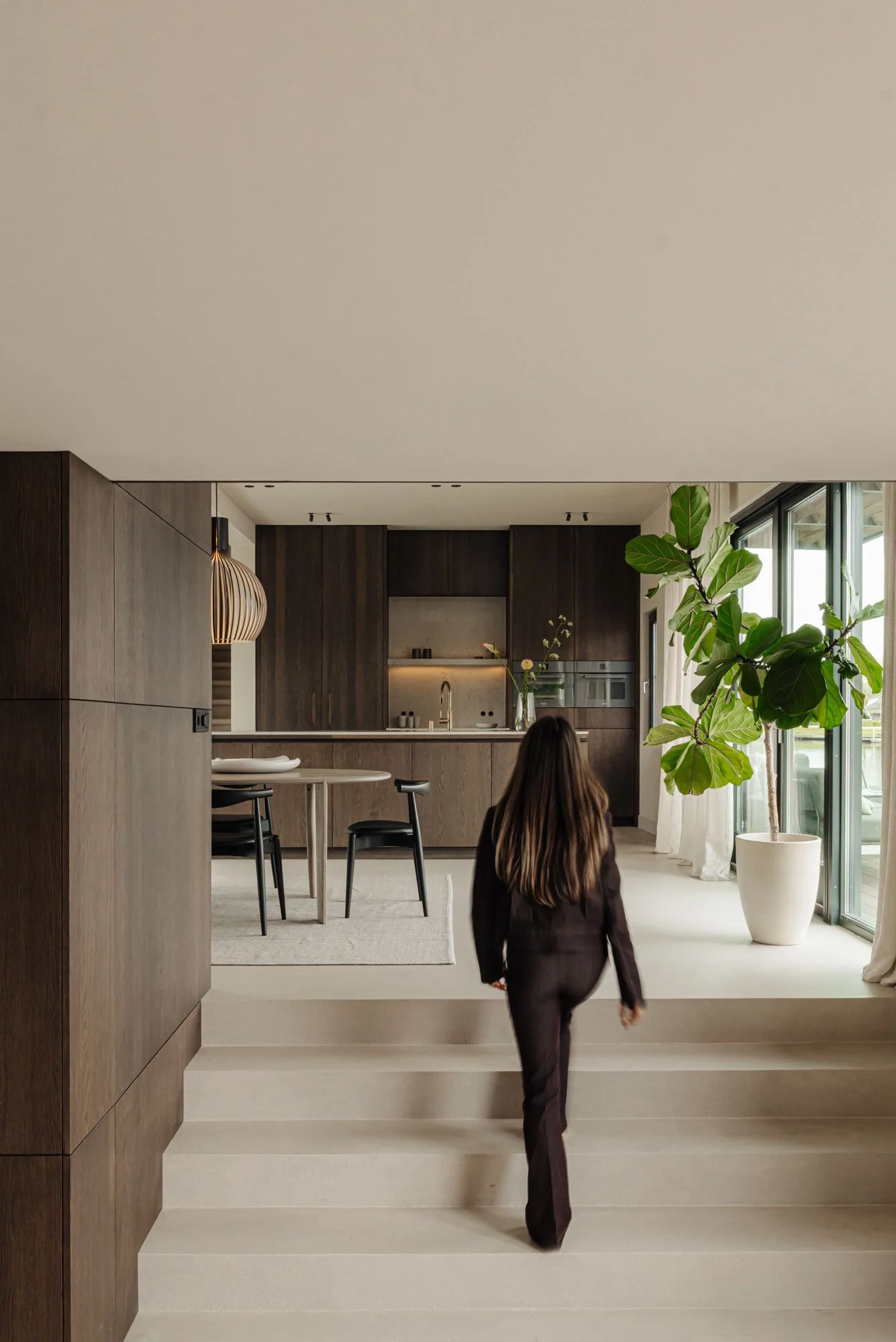 Interieurontwerper Romy Engelhard van Studio Engelhard uit Amsterdam loopt via de trap naar de leefkeuken in een high-end interieurontwerp vol ingetogen luxe.