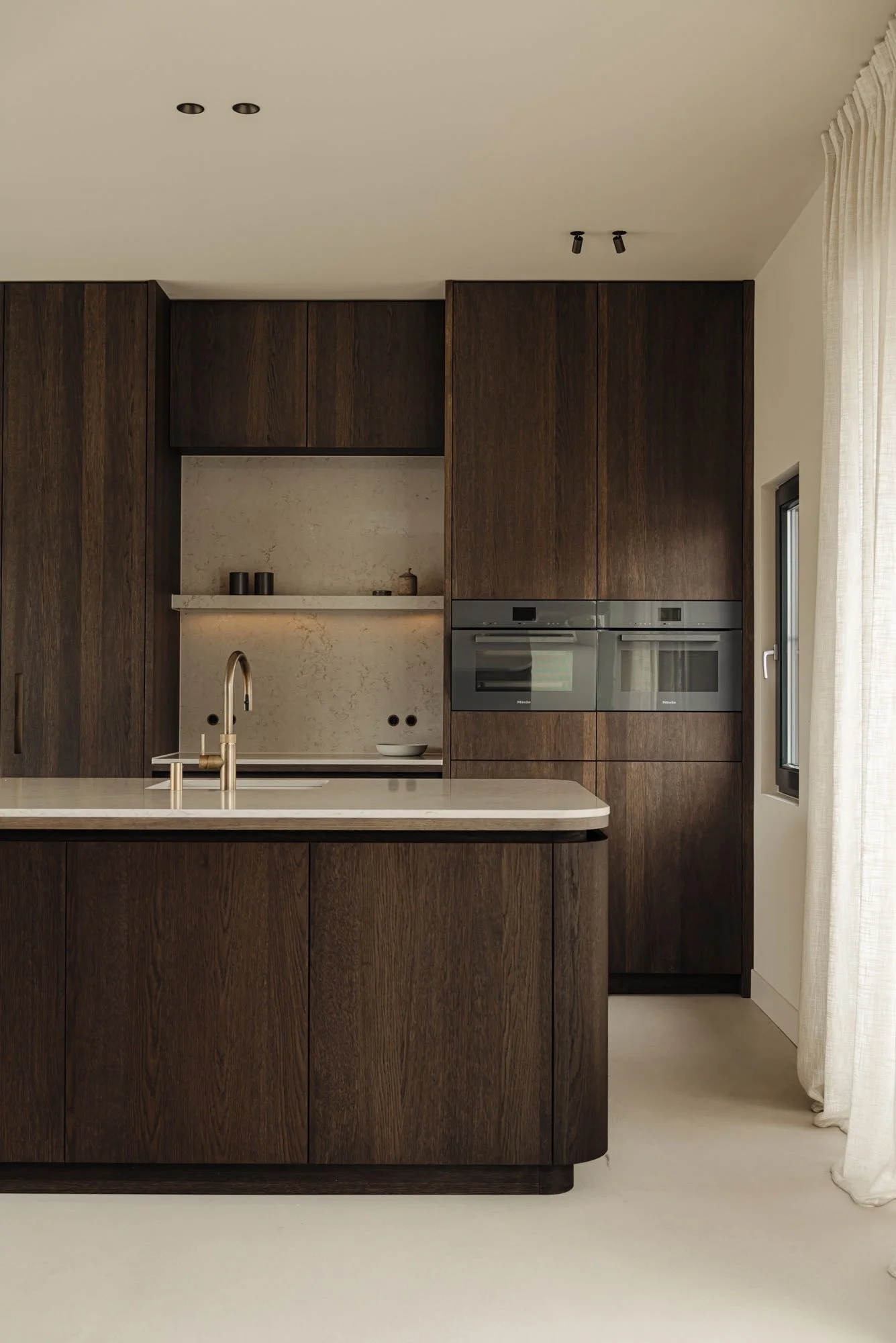 High-end keuken op maat in een luxe watervilla met een kookeiland met afgeronde hoeken, ontworpen met een sfeer van ingetogen luxe door Studio Engelhard uit Amsterdam.