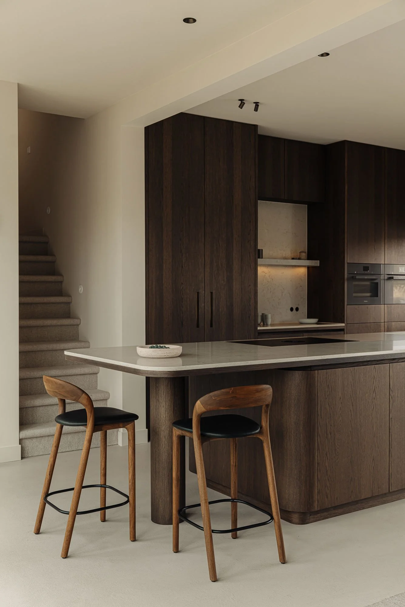 Ingetogen luxe in een high-end keukenontwerp met een maatwerk kookeiland en design barstoelen, ontworpen door Studio Engelhard van interieurontwerper Romy Engelhard uit Amsterdam.