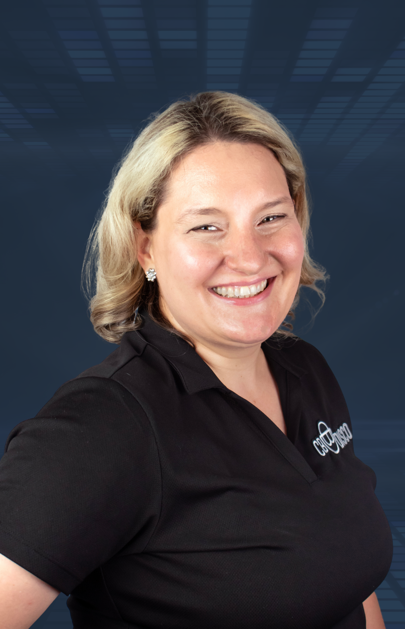 A smiling woman with shoulder-length blonde hair, wearing a black polo shirt with a logo on it, standing in front of a digital blue background.
