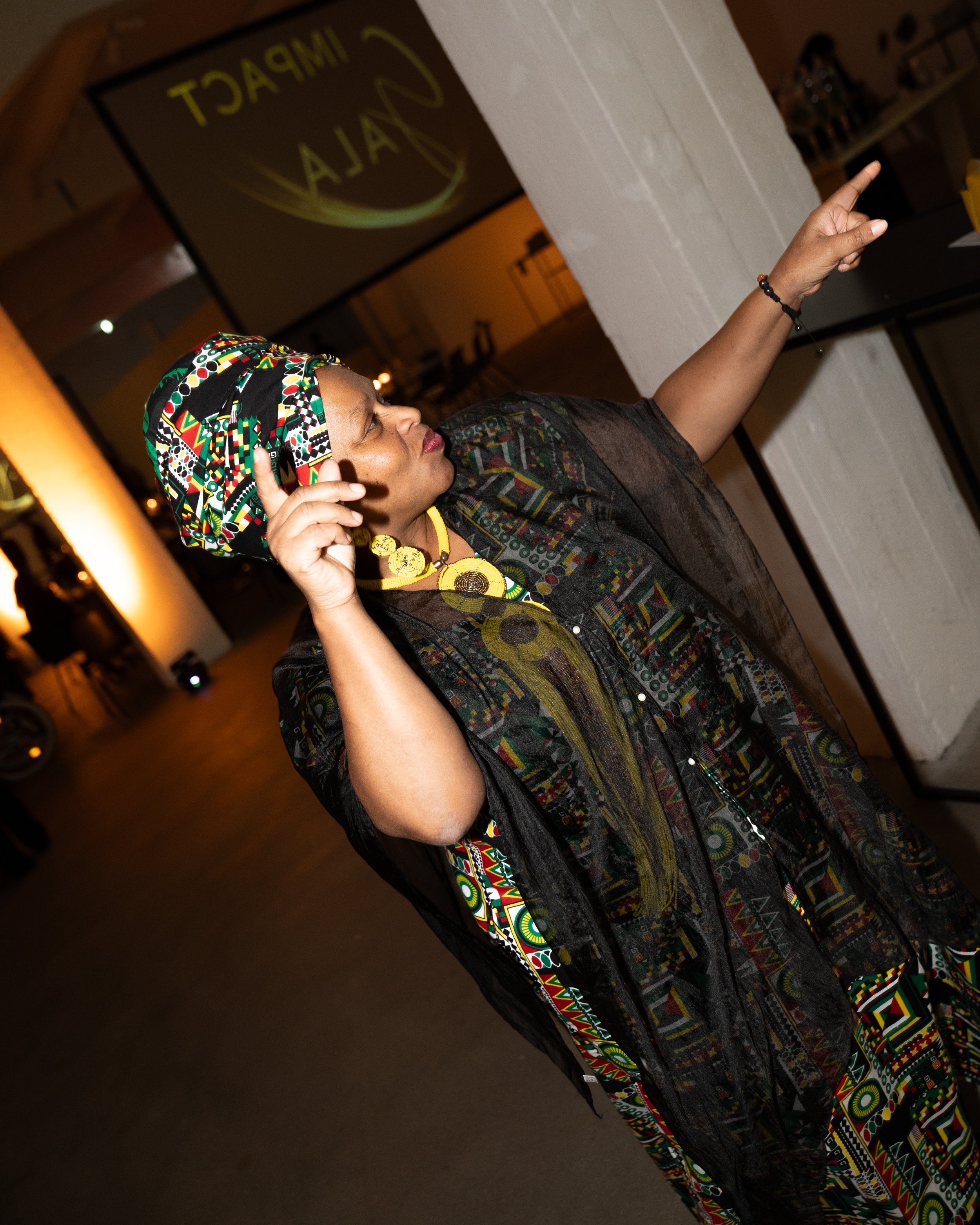 Person in colorful attire pointing, with "IMPACT NALA" projected on screen in background.