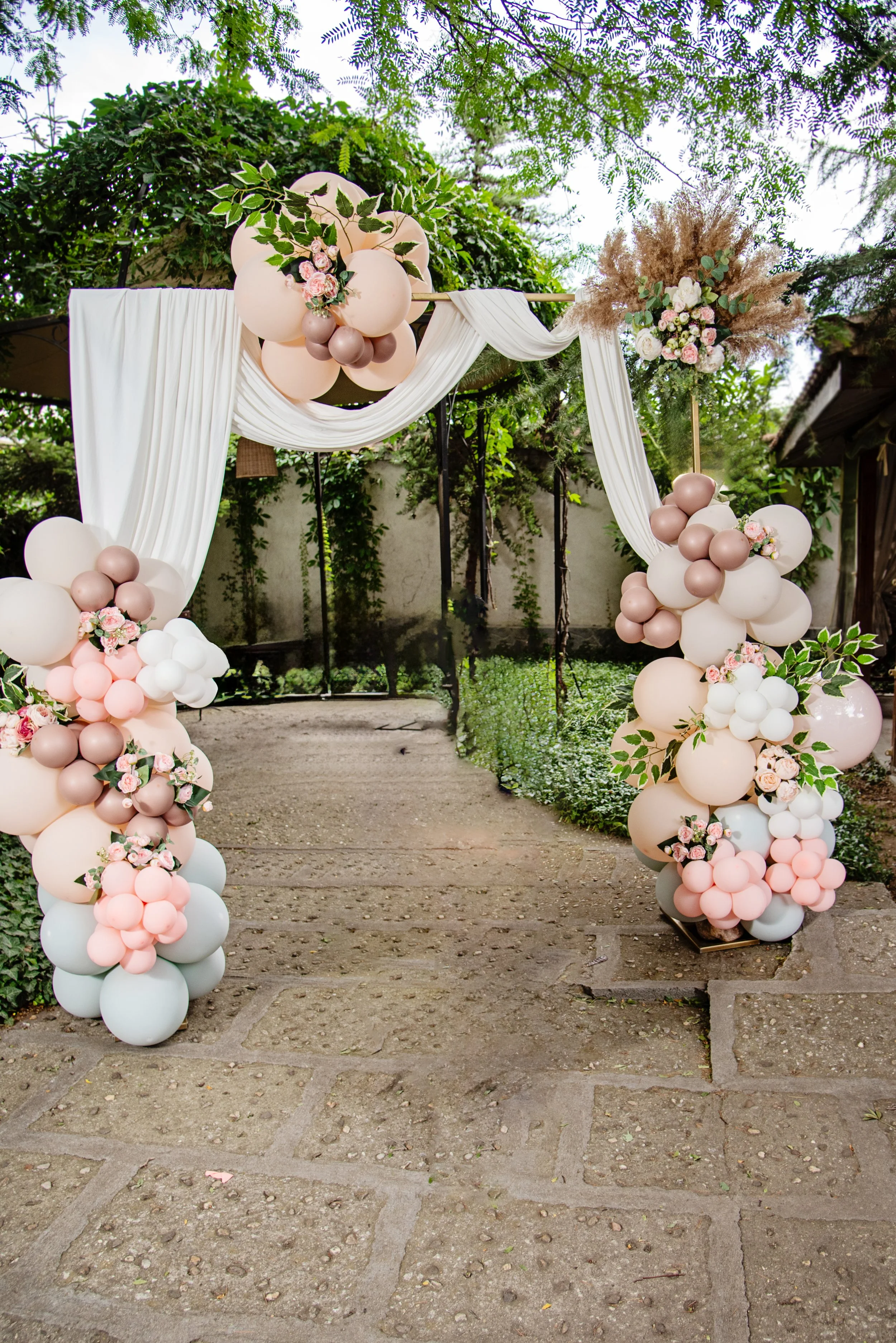 Outdoor wedding arch with pastel balloon arrangements and floral decorations.