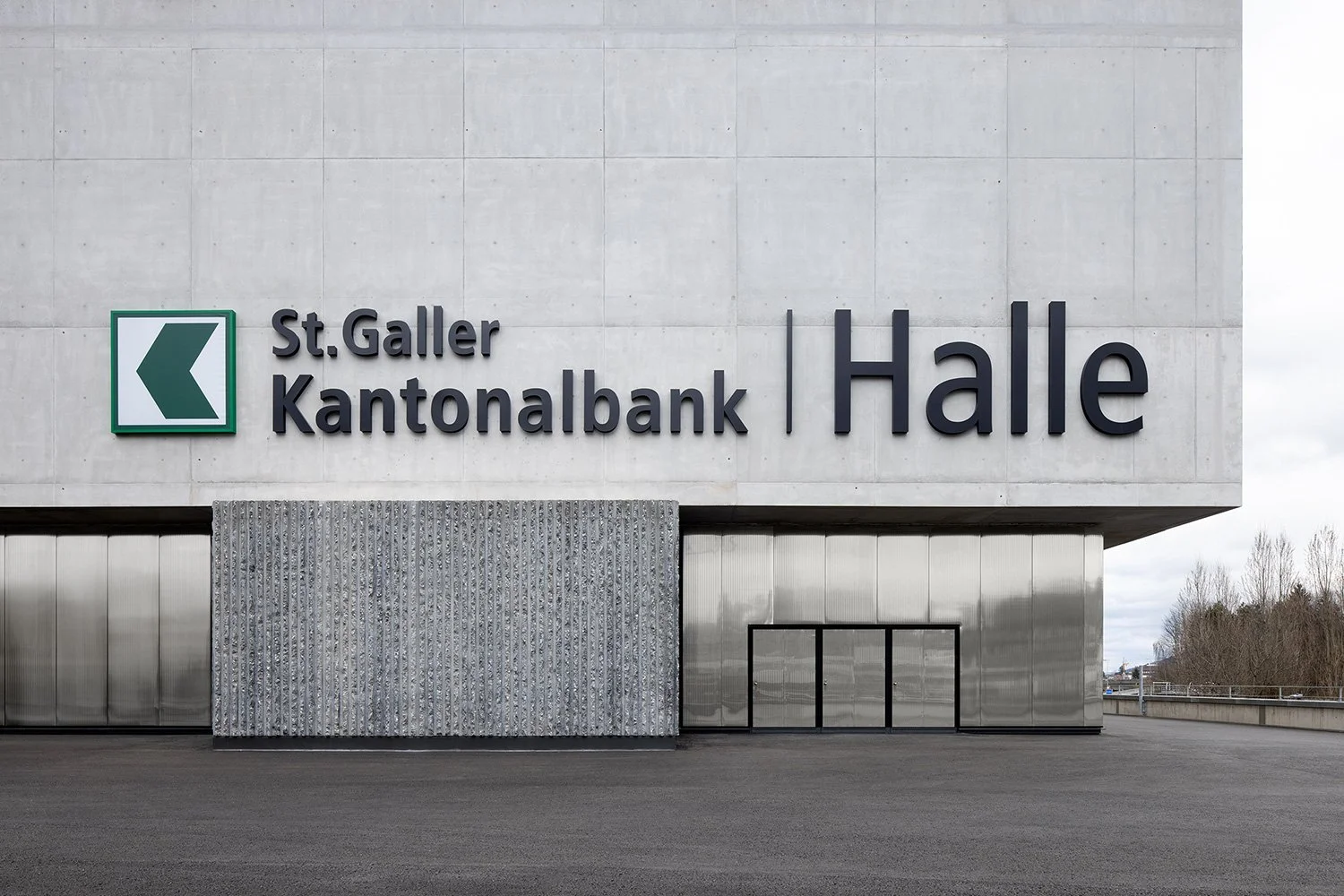 Außenaufnahme der SGKB Halle in St. Gallen mit markanter Betonfassade und großformatigem Schriftzug der St. Galler Kantonalbank Halle.
