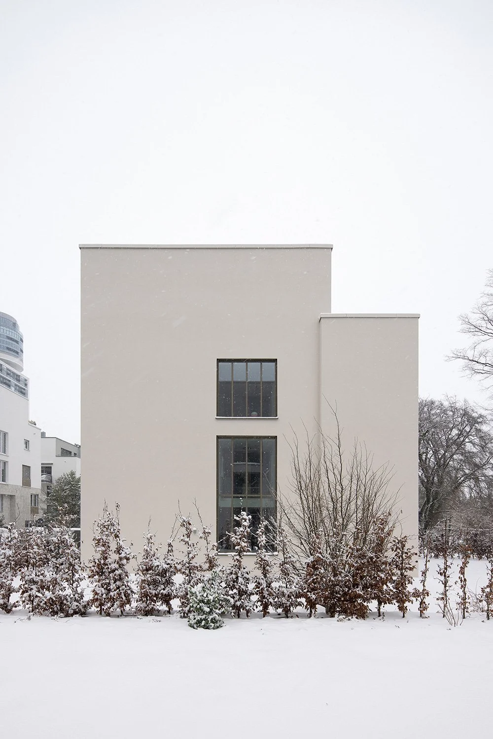 Atmosphäre.Seitenansicht eines Wohnhauses von Bilger Fellmeth Architekten mit vertikaler Fensteranordnung, heller Putzfassade und verschneiter Gartenlandschaft in Frankfurt-Sachsenhausen.
