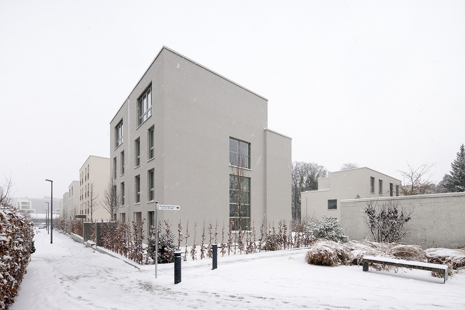 Winterliche Straßenansicht der Wohnhäuser am Schubertschen Park in Frankfurt mit vertikal gegliederten Baukörpern, reduzierter Architektur und verschneiter Freiraumgestaltung.
