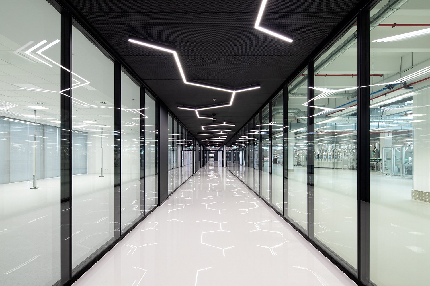 Zentralperspektivischer Verbindungsflur der Engelbert Strauss CI Factory mit Präsentationsflächen und Blick durch die gläserne Wand in die futuristisch wirkende Schuhproduktion.
