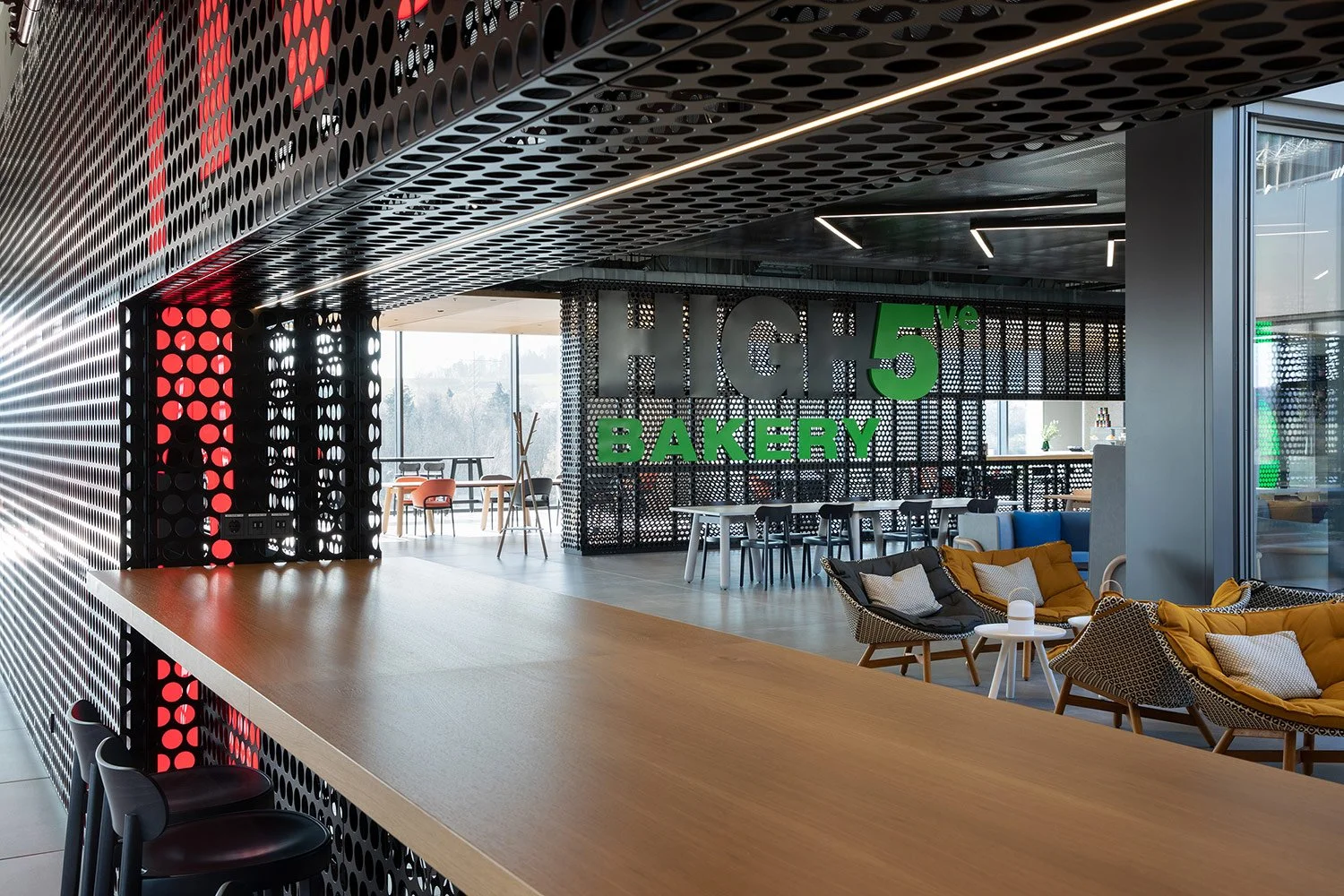Bakery- und Cafébereich der High5 Gastronomie in der Engelbert Strauss CI Factory mit schwarzer Metallstruktur, großformatiger Typografie und DEDON MBRACE Sesseln von Sebastian Herkner.
