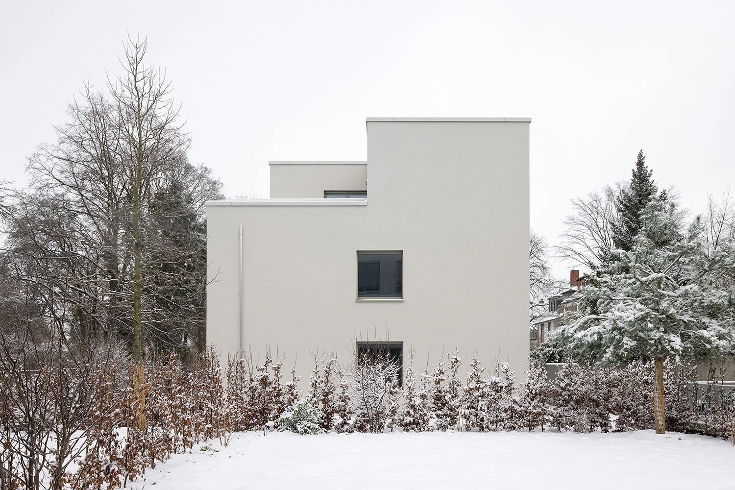 Architekturfotografie eines Wohnhauses am Schubertschen Park mit gestaffelter Baukörperkomposition, heller Fassadenfarbe und altem Baumbestand im winterlichen Außenraum.
