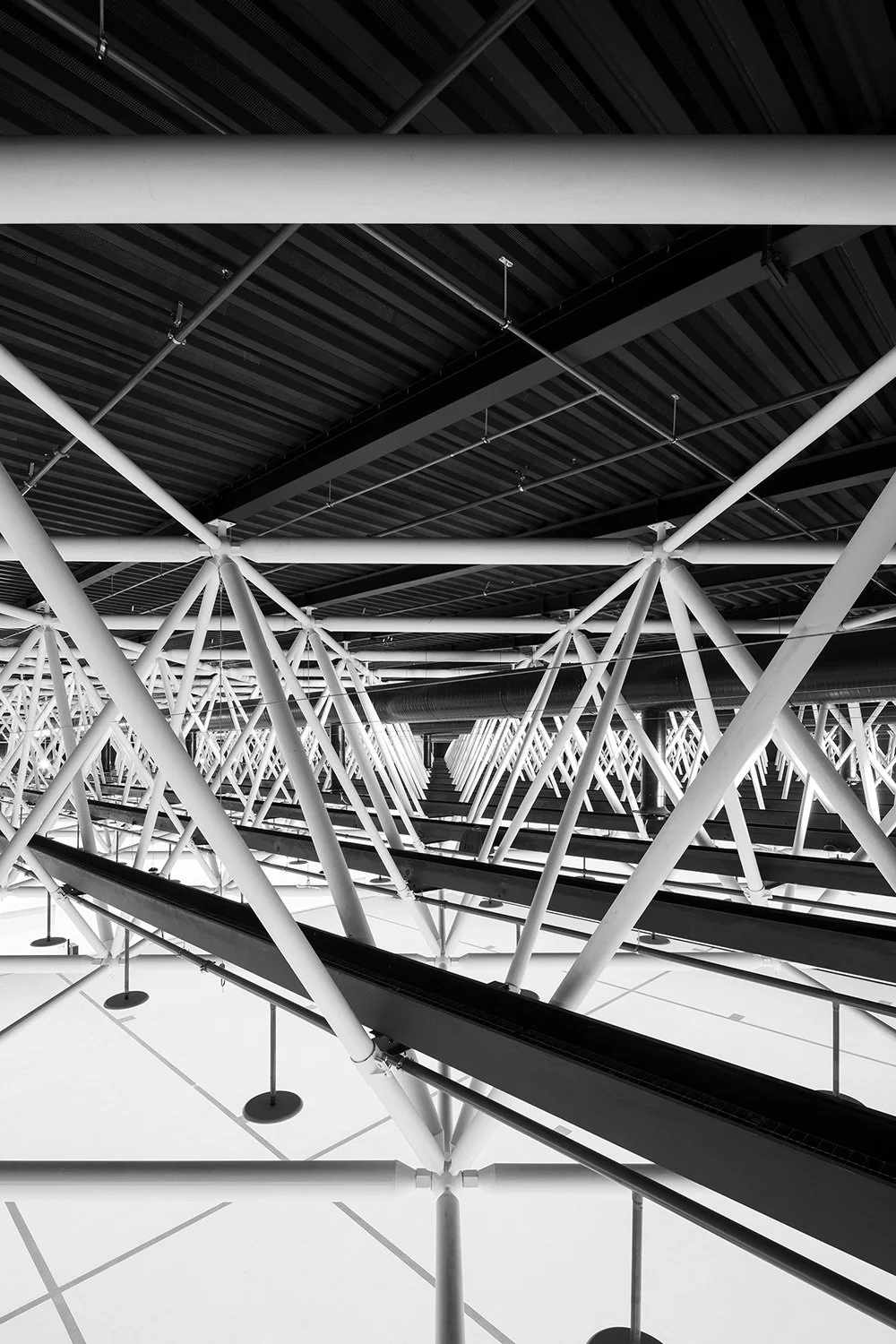 Weiter Blick durch die Dachkonstruktion der SGKB Halle St. Gallen mit schwarzer Dachfläche, dichter weißer Stahlstruktur und sichtbarem Hallenboden.
