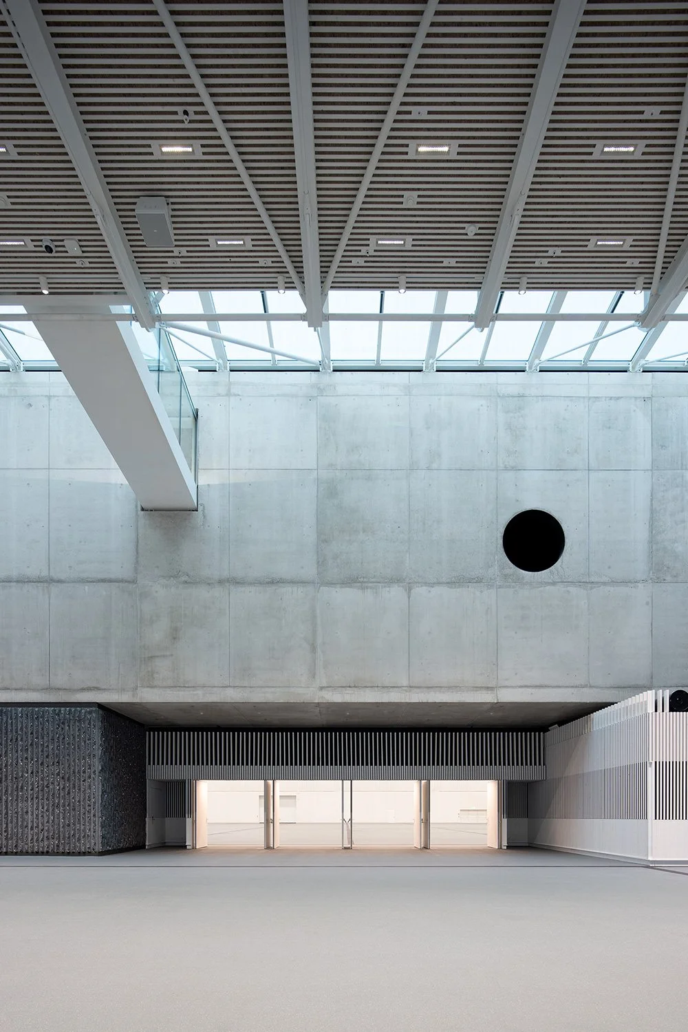 Innenraumaufnahme des Foyers der SGKB Halle St. Gallen mit Lichtdecke, Sichtbetonwand und Blick in die Eventhalle.
