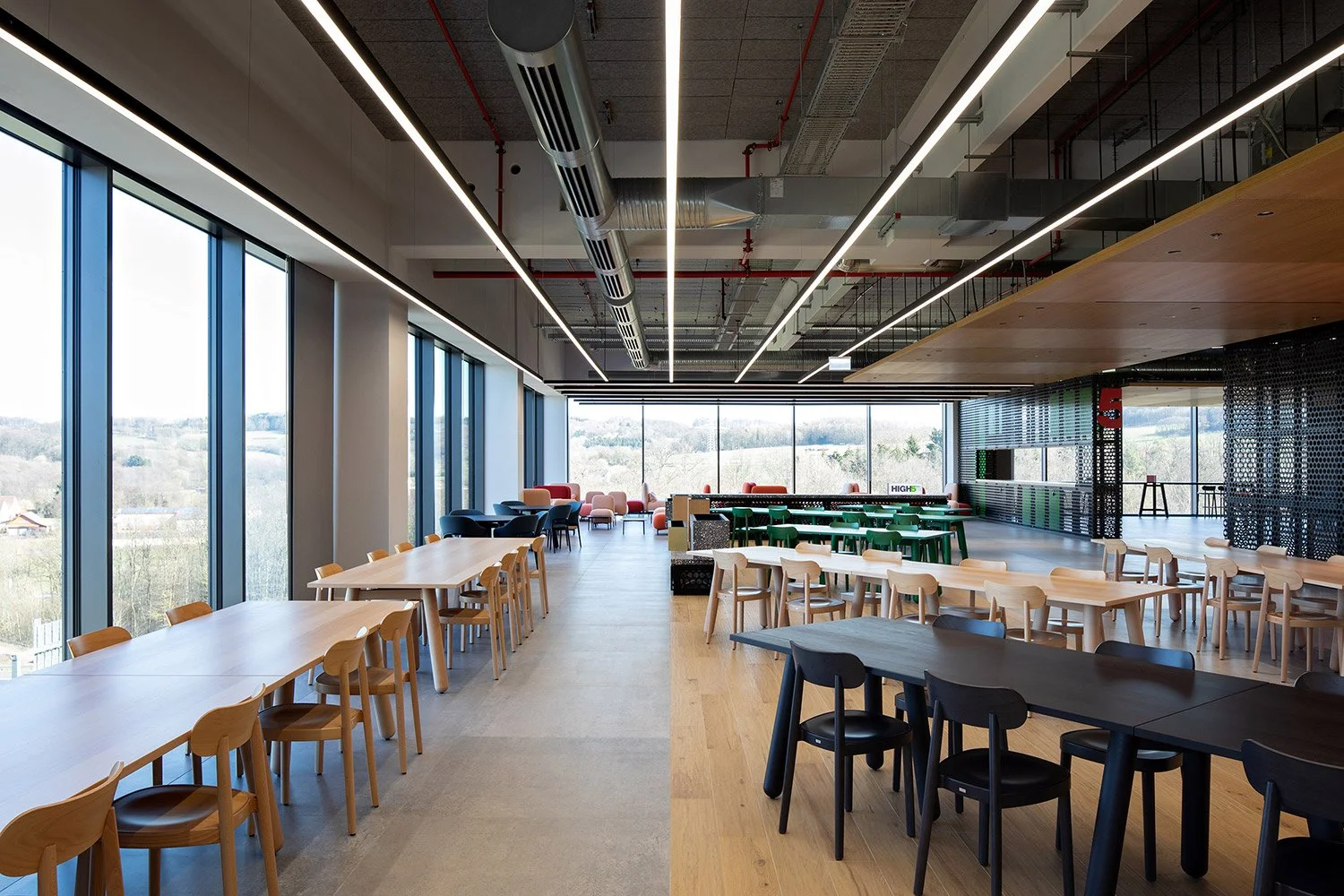 Weitwinkelaufnahme der High5 Mensa in der Engelbert Strauss CI Factory mit langen Tischreihen, raumhoher Verglasung und Thonet-Holzstühlen des Modells 118.
