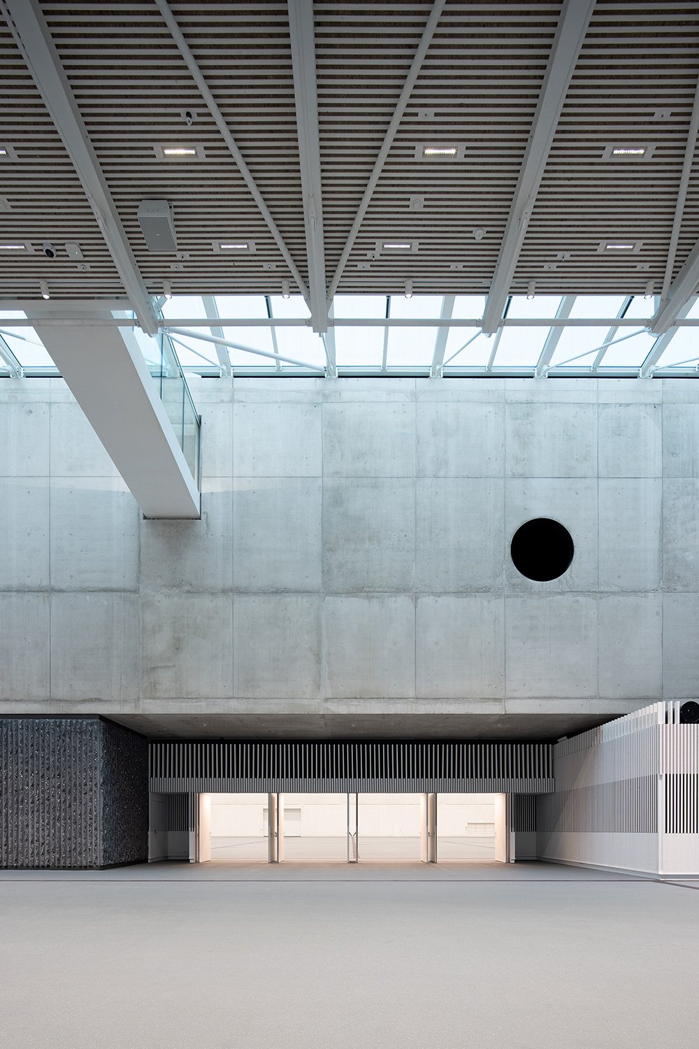 Innenraumaufnahme des Foyers der SGKB Halle St. Gallen mit Lichtdecke, Sichtbetonwand und Blick in die Eventhalle.
