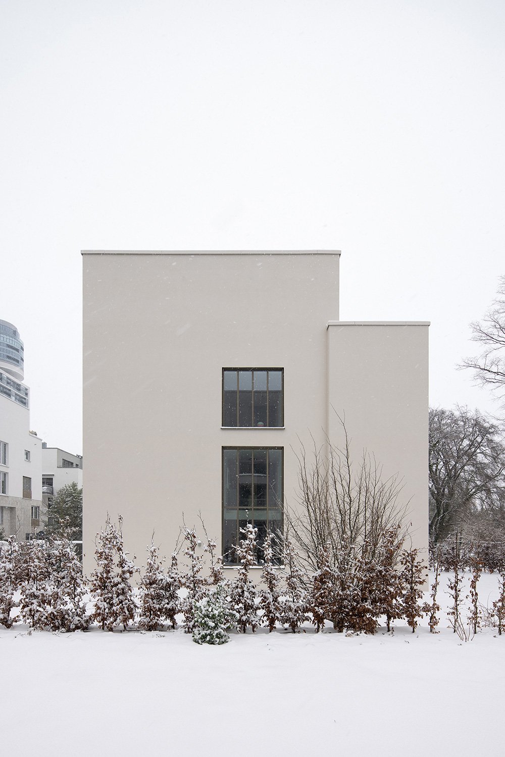 Atmosphäre.Seitenansicht eines Wohnhauses von Bilger Fellmeth Architekten mit vertikaler Fensteranordnung, heller Putzfassade und verschneiter Gartenlandschaft in Frankfurt-Sachsenhausen.