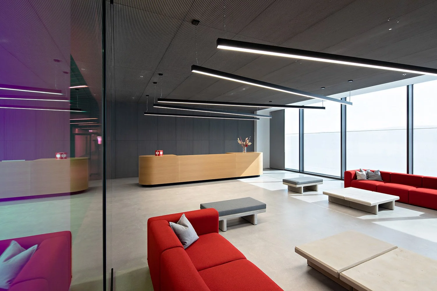 Moderner Lounge- und Empfangsbereich der Engelbert Strauss CI Factory mit roten Sofas, warmen Holzoberflächen und minimalistischer Innenarchitektur.
