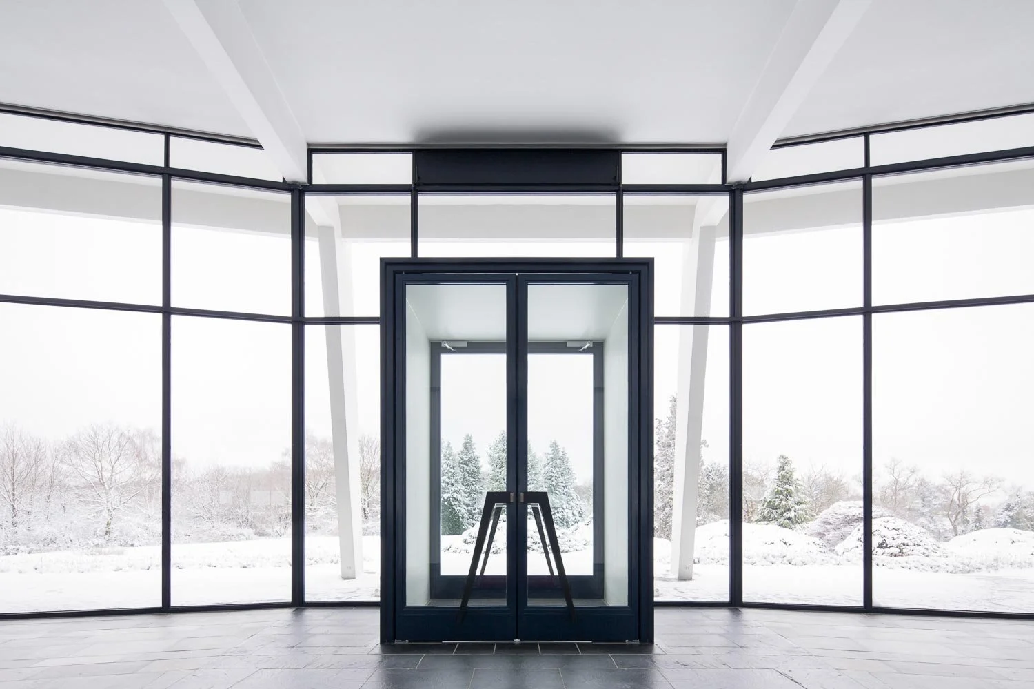 Interieur-Aufnahme des Eingangs zum Foyer des Bahá'í Haus der Andacht. Der Blick durch die minimalistische Glasfront und die gläsernen Flügeltüren in die Landschaft unterstreicht die Offenheit des Entwurfs.